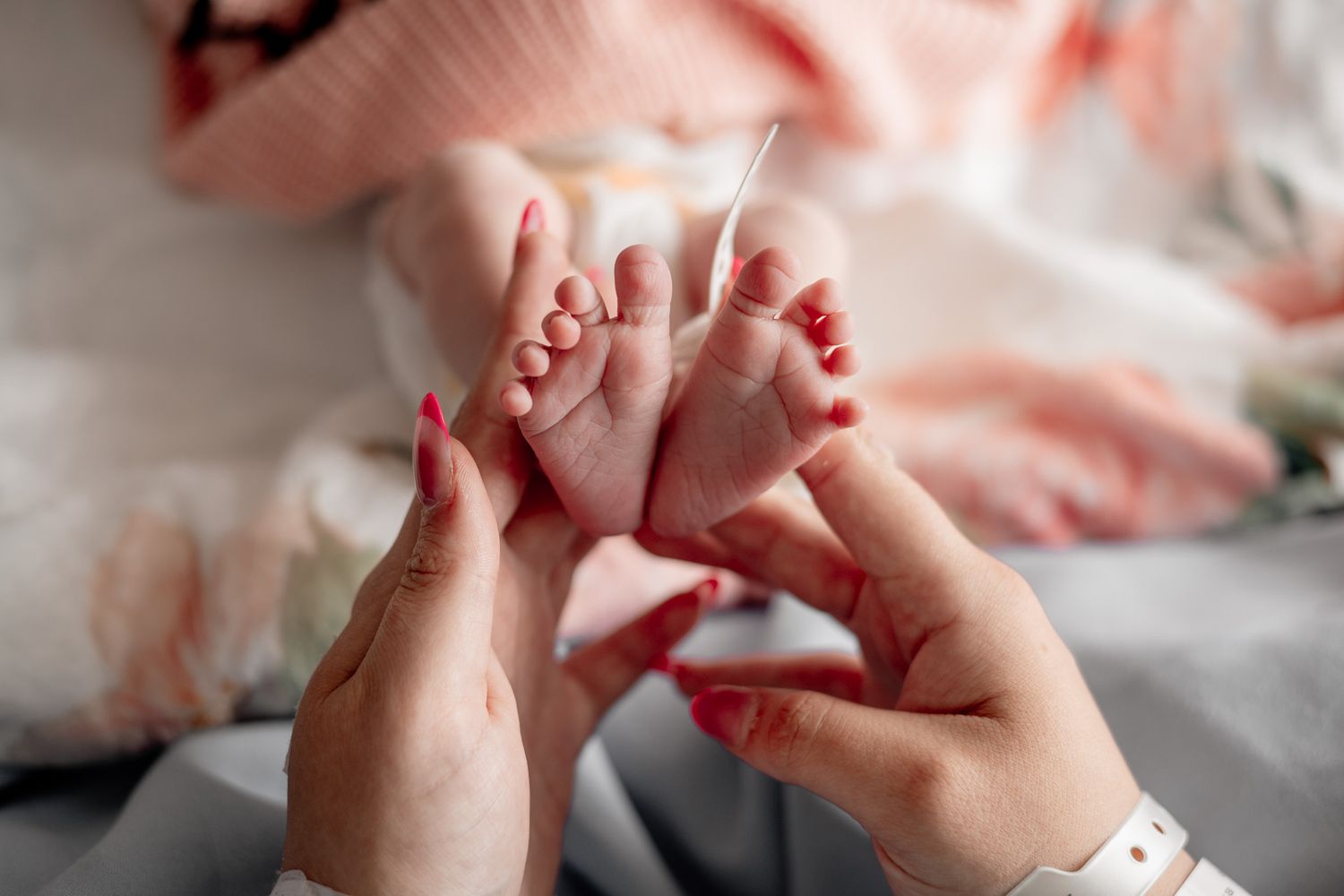 Hands performing a gentle baby foot massage on soft white bedding.
