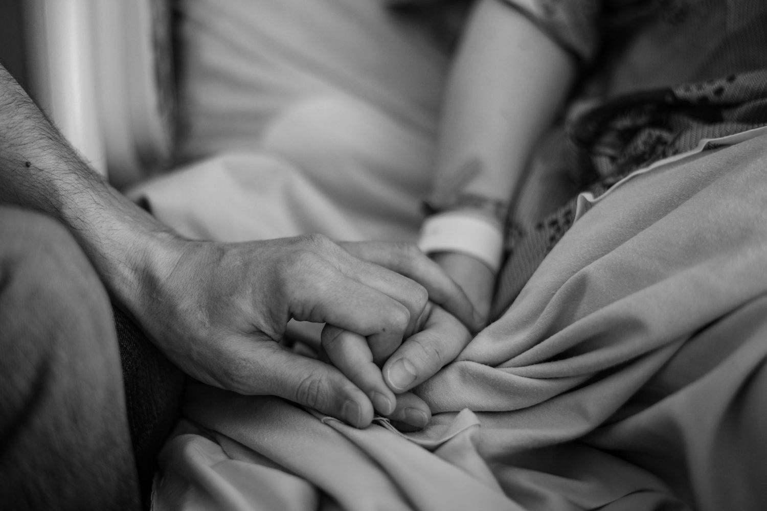Black and white close-up photo showing hands tenderly holding a newborn baby wrapped in soft fabric.