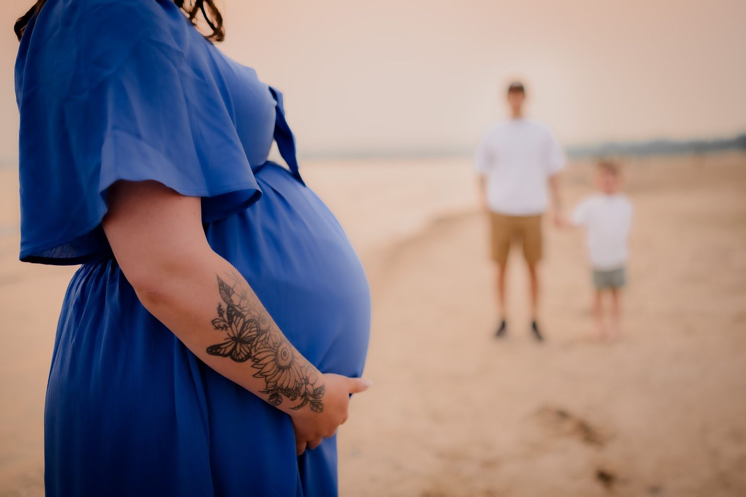 Beach maternity photos at sunset featuring a flowing blue dress against sandy backdrop. Maternity photographer Ontario