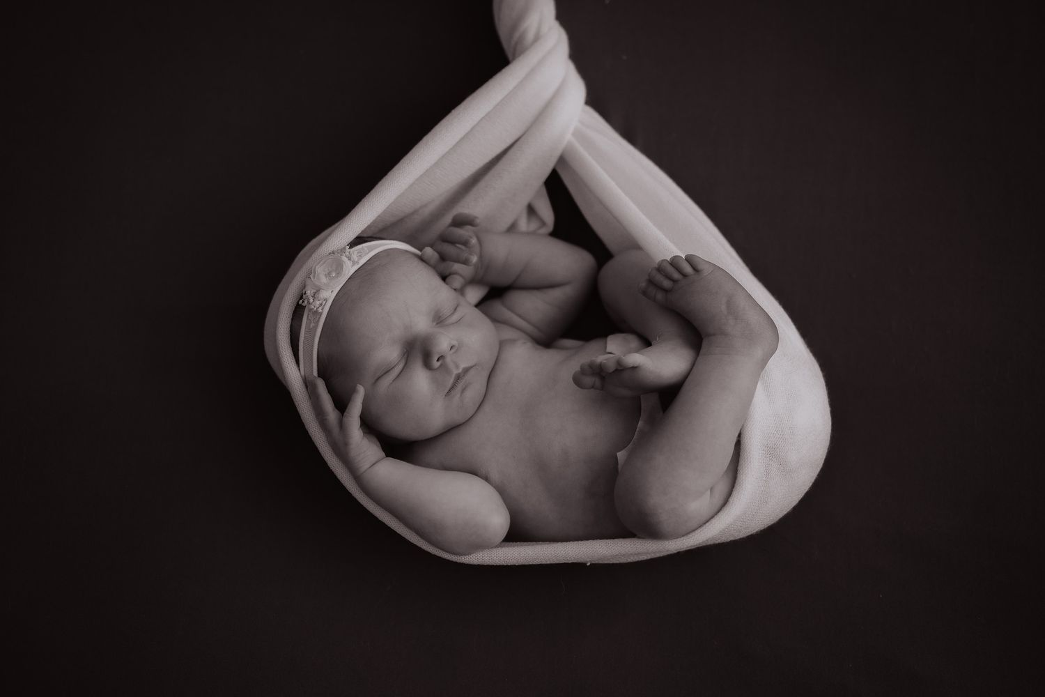 Series of black and white portraits showing a sleeping newborn in white swaddling.