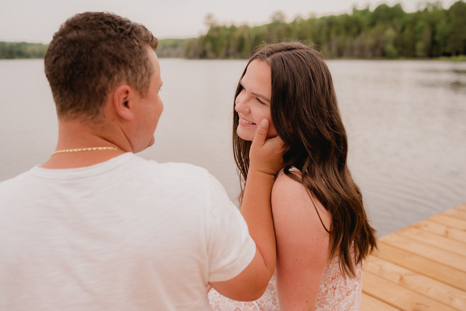 A couple shares a romantic moment on a wooden dock by a serene lake during sunset.