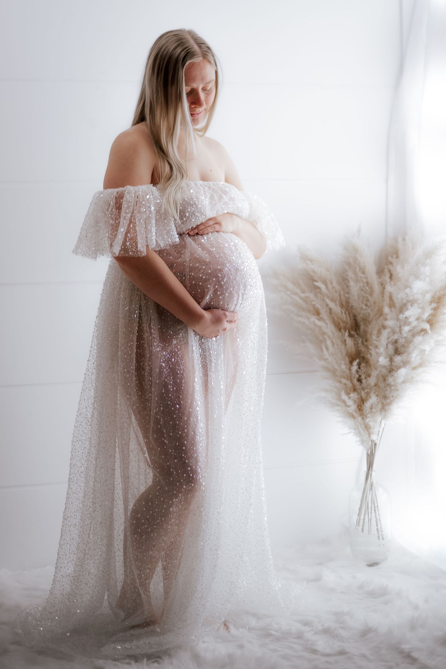 Ethereal maternity photoshoot featuring flowing white lace gown against bright studio backdrop with pampas grass. Maternity photographer Ont