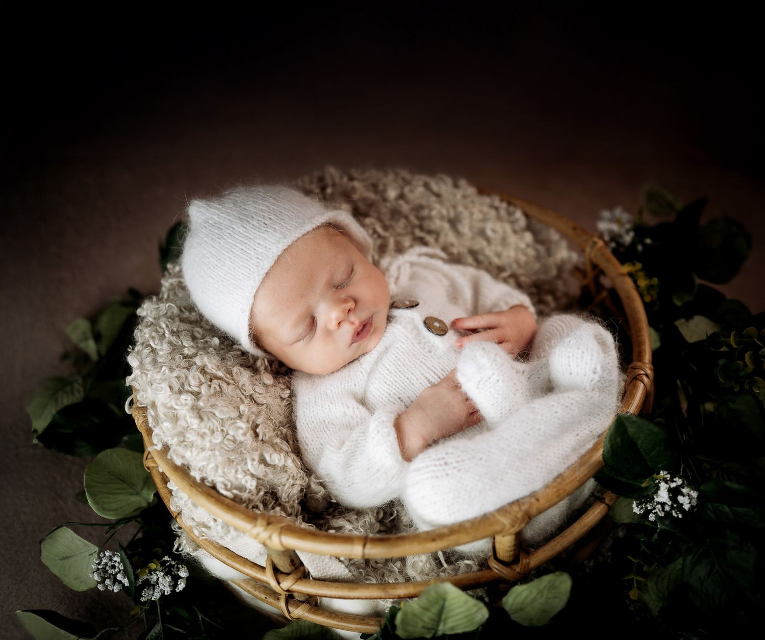 Newborn baby sleeping peacefully on a rustic wooden surface surrounded by delicate green foliage and white fabric.