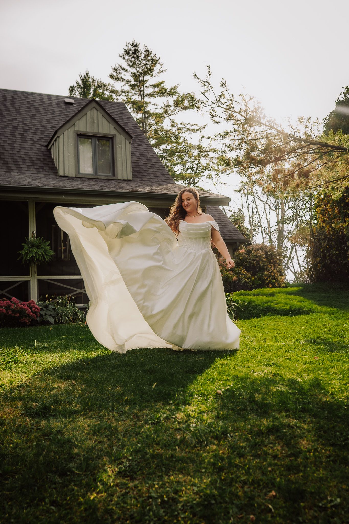 White flowing fabric billows in the wind on a grassy hillside with a house in the background during golden hour.