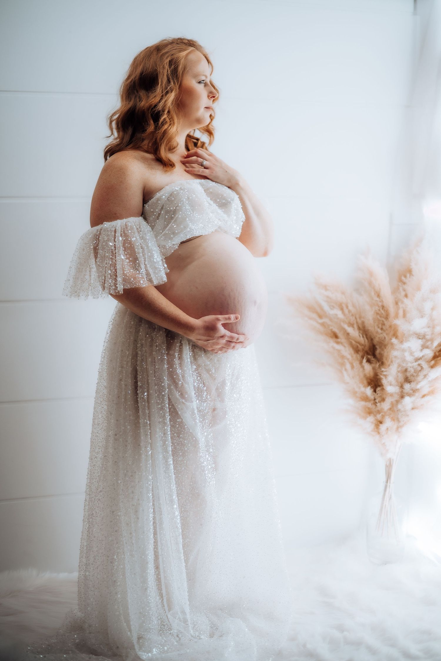 Ethereal maternity photos in white lace gown with flowing fabric against bright studio backdrop. Maternity photographer Ontario