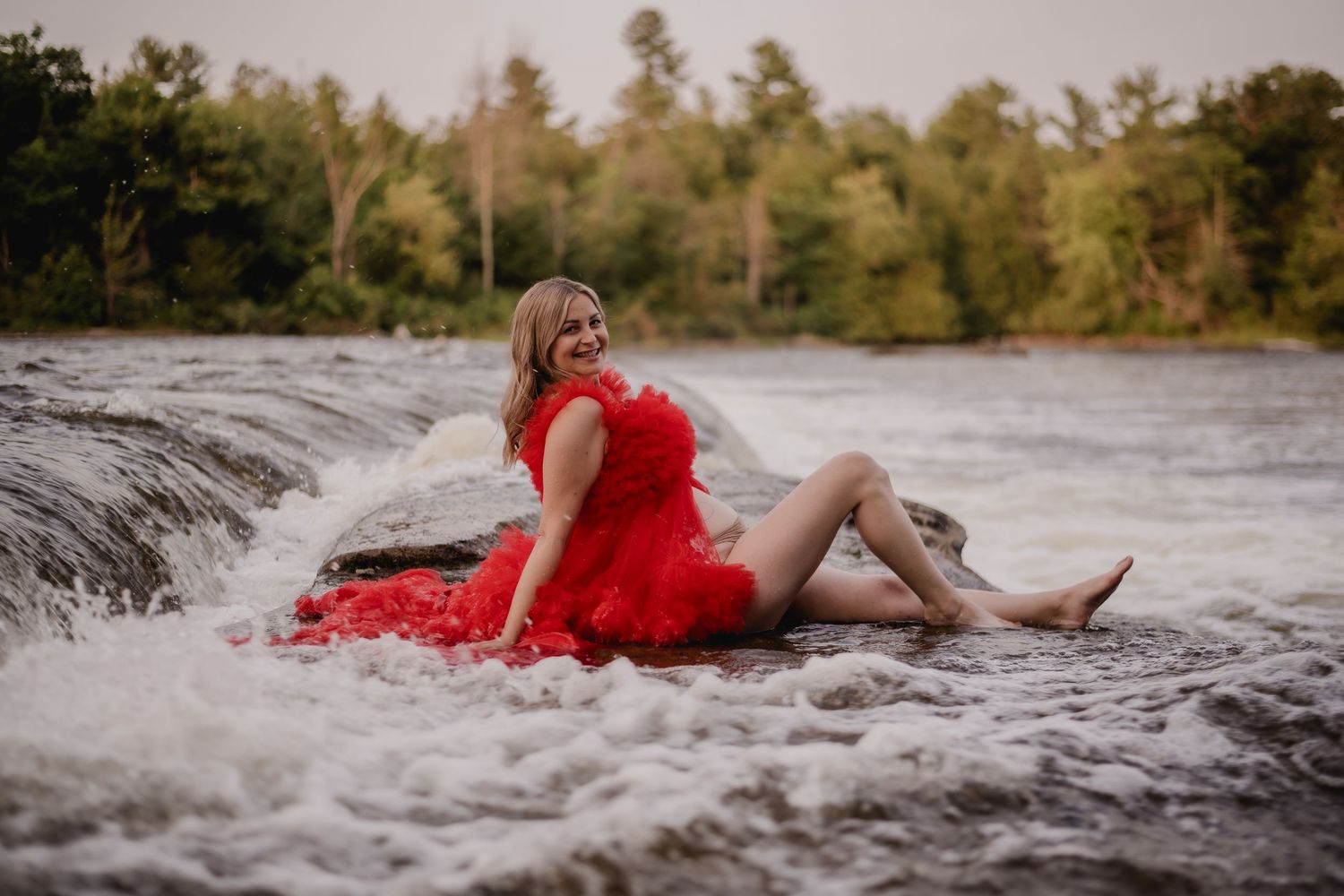 A dramatic portrait featuring a red dress against flowing water and natural rock formations. Maternity photographer Ontario