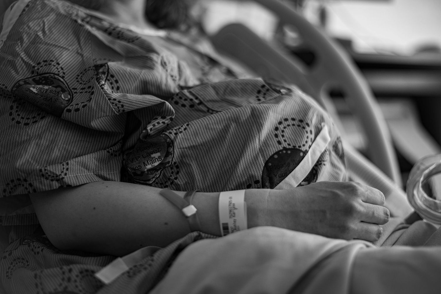 Side view of pregnant paitent resting in hospital bed with medical equipment. Birth Photographer Ontario