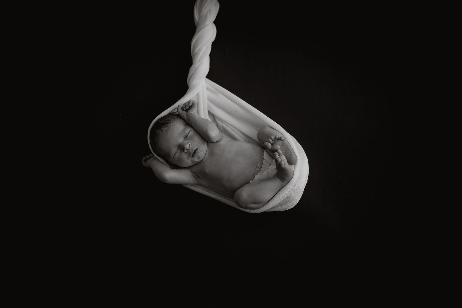 Minimalist black and white newborn portrait with dramatic lighting and soft wrapping.