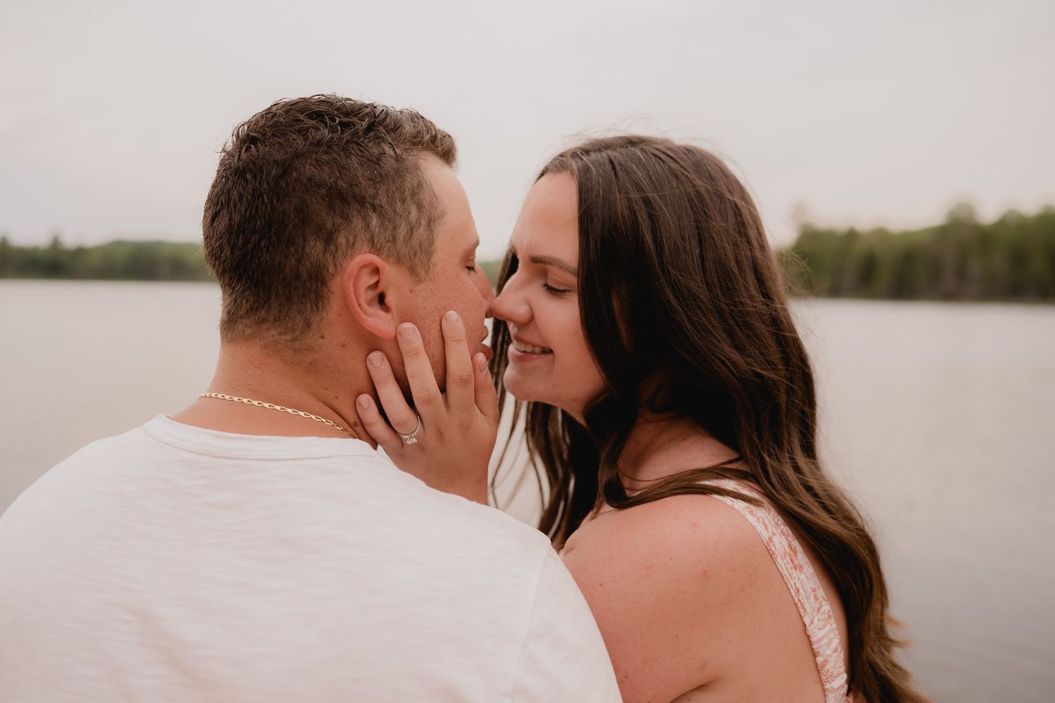 Romantic couple embraces on a sandy beach at sunset beside a tranquil lake.