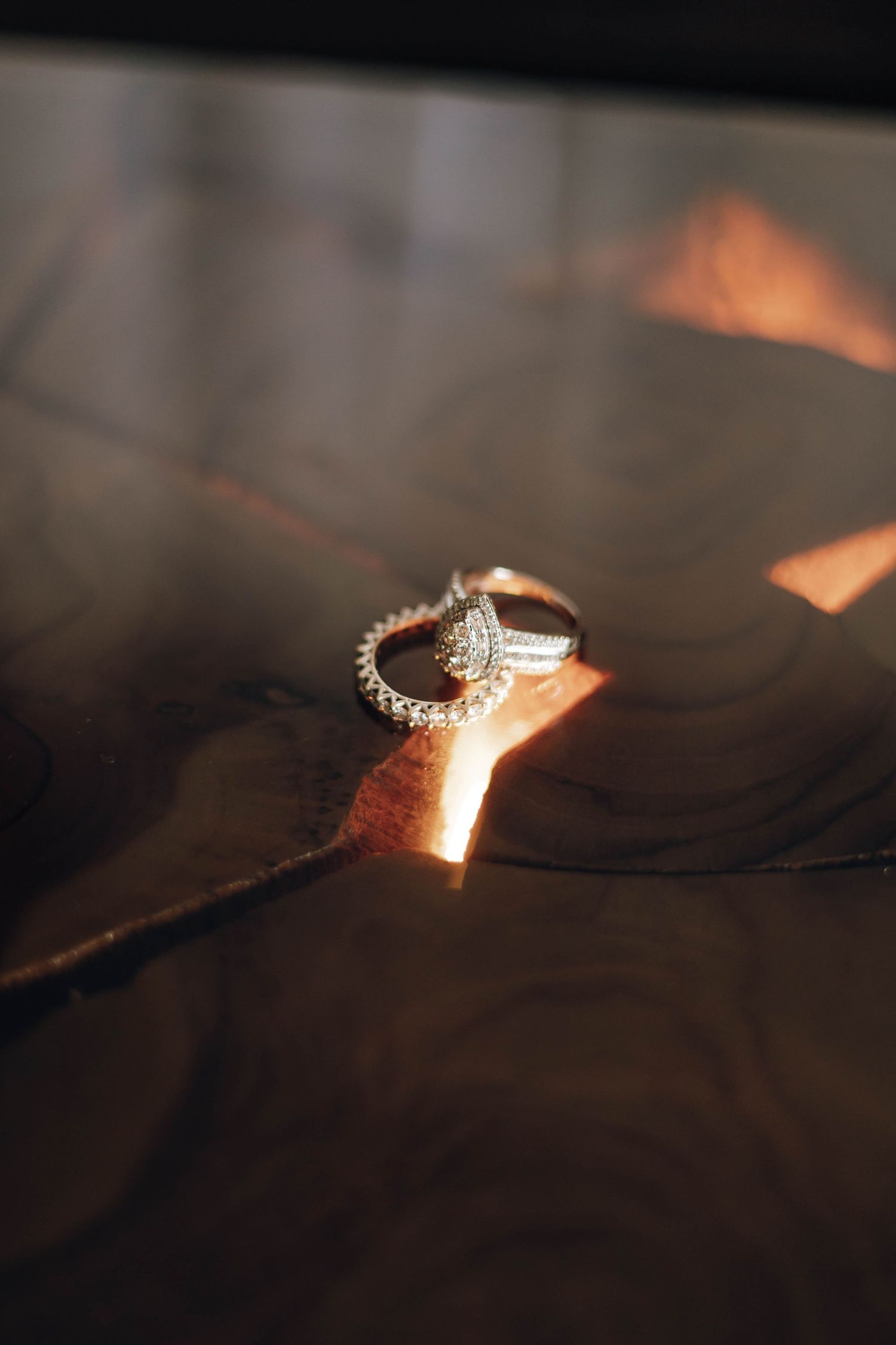 Diamond engagement ring and wedding band set displayed on a dark reflective surface with warm golden light.