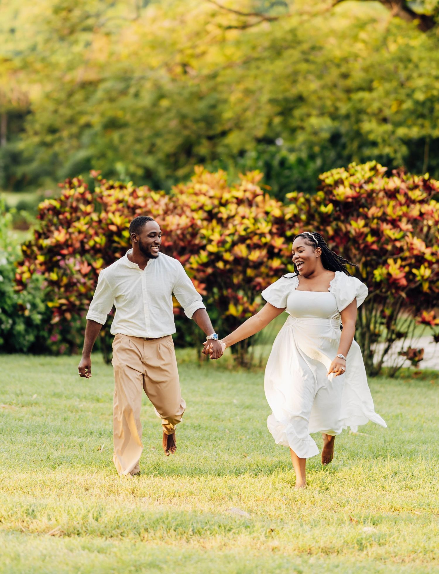 A joyful Black couple runs hand-in-hand across a lush green lawn, surrounded by vibrant autumn foliage.