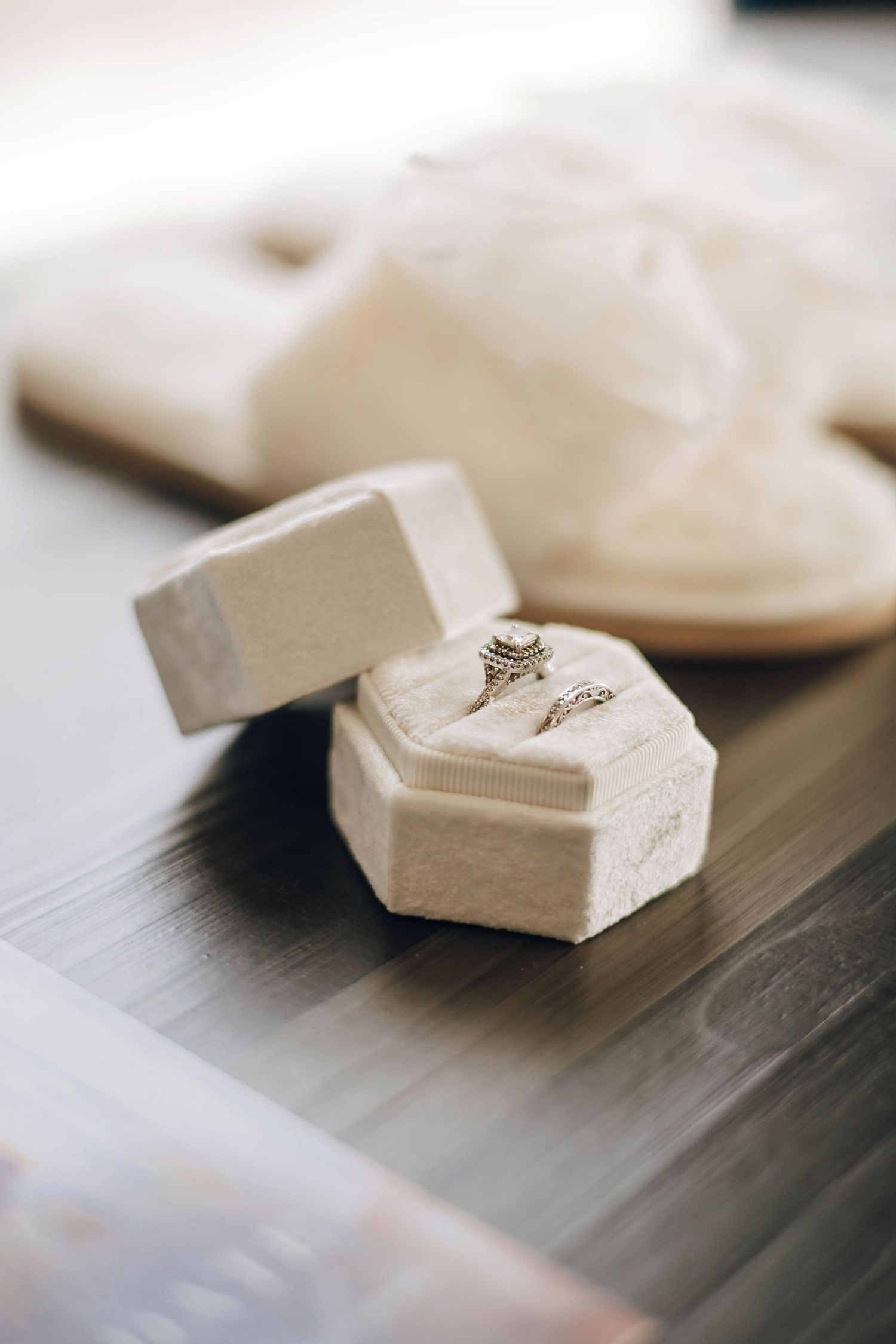 Two diamond wedding rings displayed in an elegant cream velvet octagonal ring box on a wooden surface.