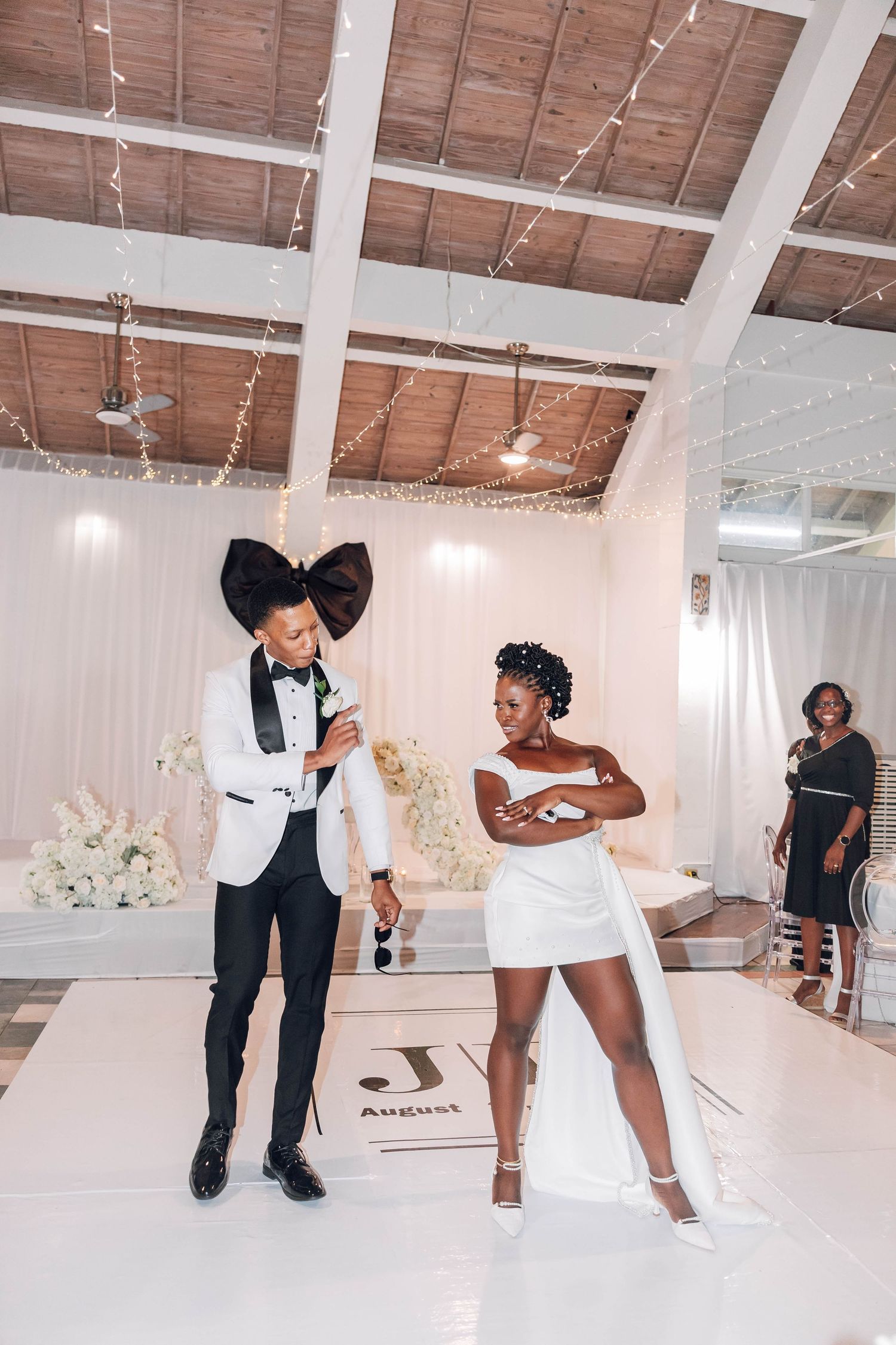 A bride and groom share a joyful first dance on a white monogrammed dance floor at an elegant wedding reception.