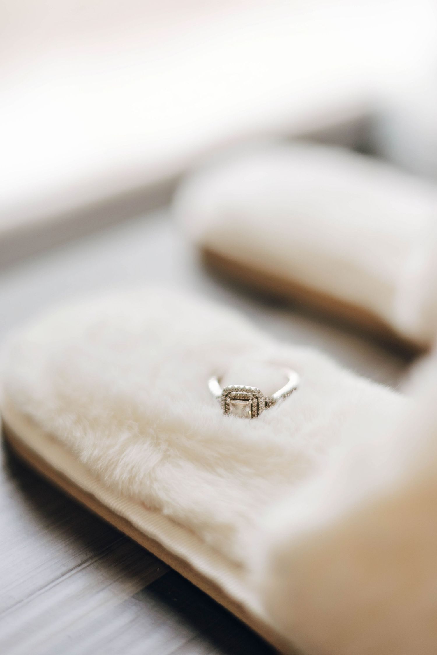 Elegant diamond engagement ring displayed on a soft cream velvet jewelry box on a wooden surface.