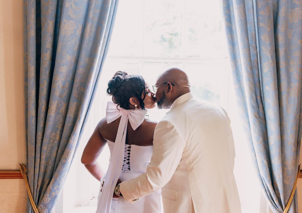 A bride and groom share a romantic kiss in front of elegant blue curtains during their wedding ceremony.