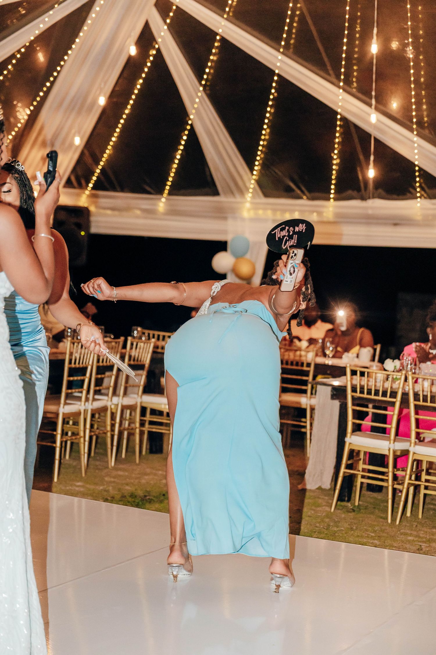 Woman in light blue dress dancing energetically at an elegant wedding reception under a tent with string lights.