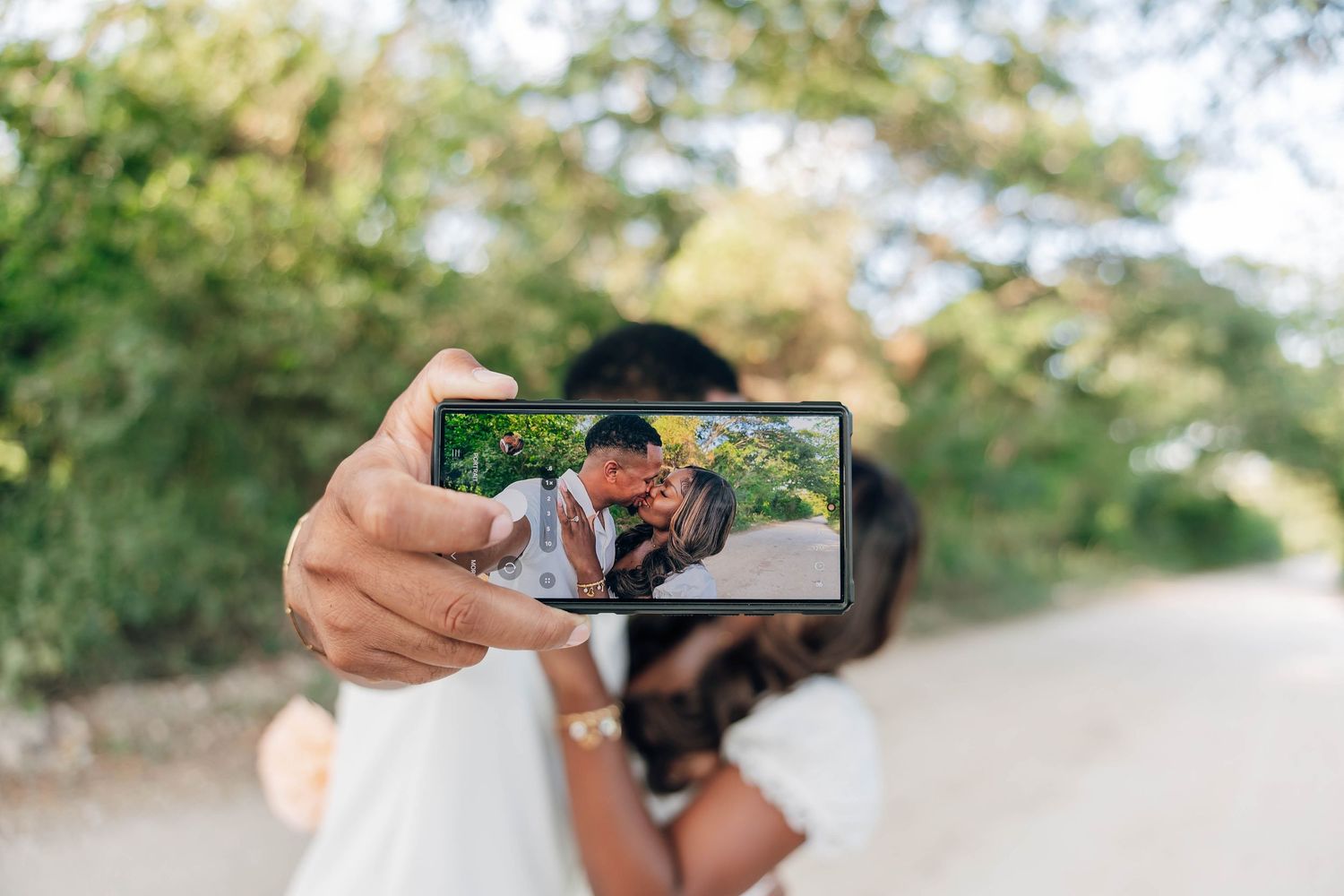 Couple taking a romantic selfie on a smartphone outdoors, capturing their kiss on the phone screen.