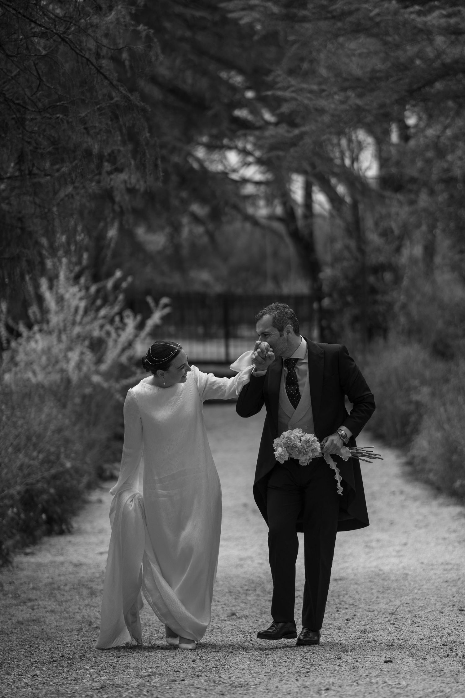 A tender black and white moment between newlyweds walking along a garden path.