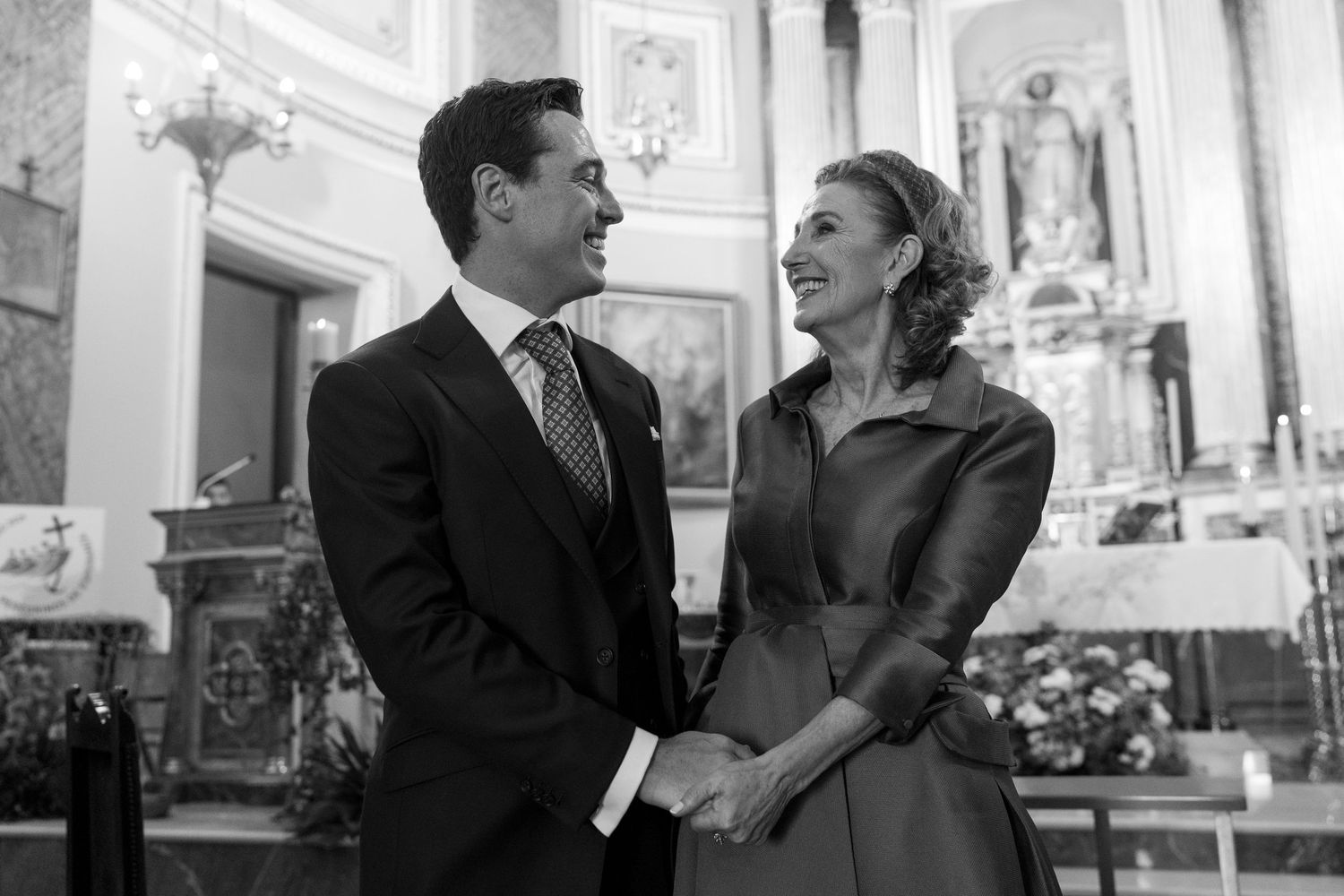 A black and white photo showing guests seated in formal attire during a wedding ceremony in an ornate setting.