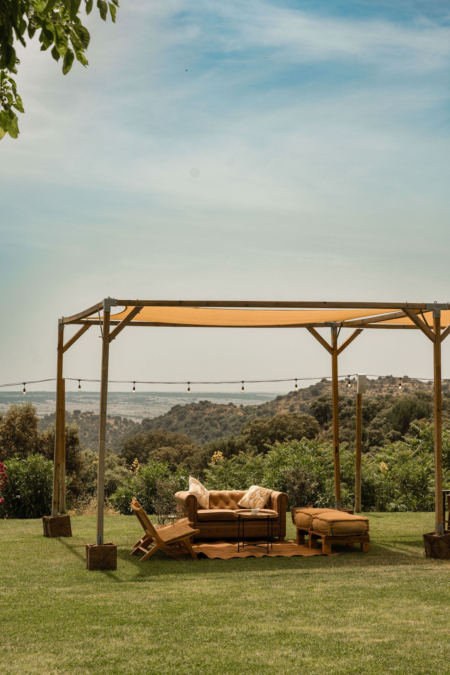 Rustic wooden pergola with lounge furniture set up on grassy hilltop for outdoor wedding reception.