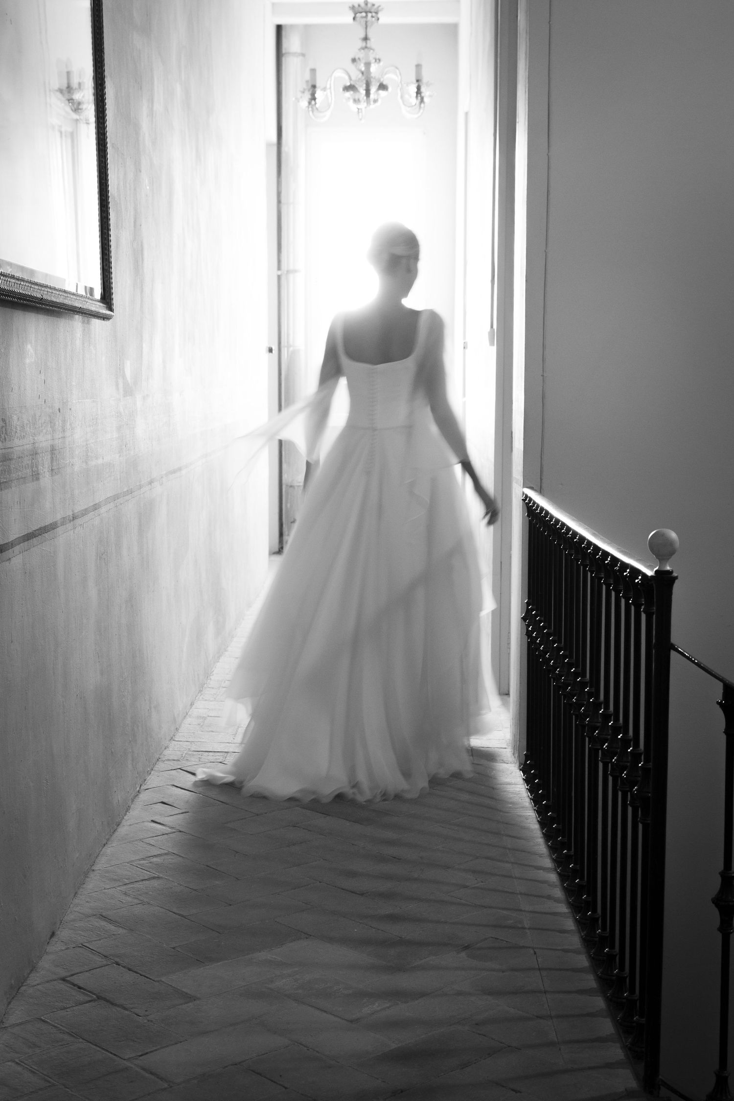 Backlit silhouette of wedding dress in hallway with chandelier.