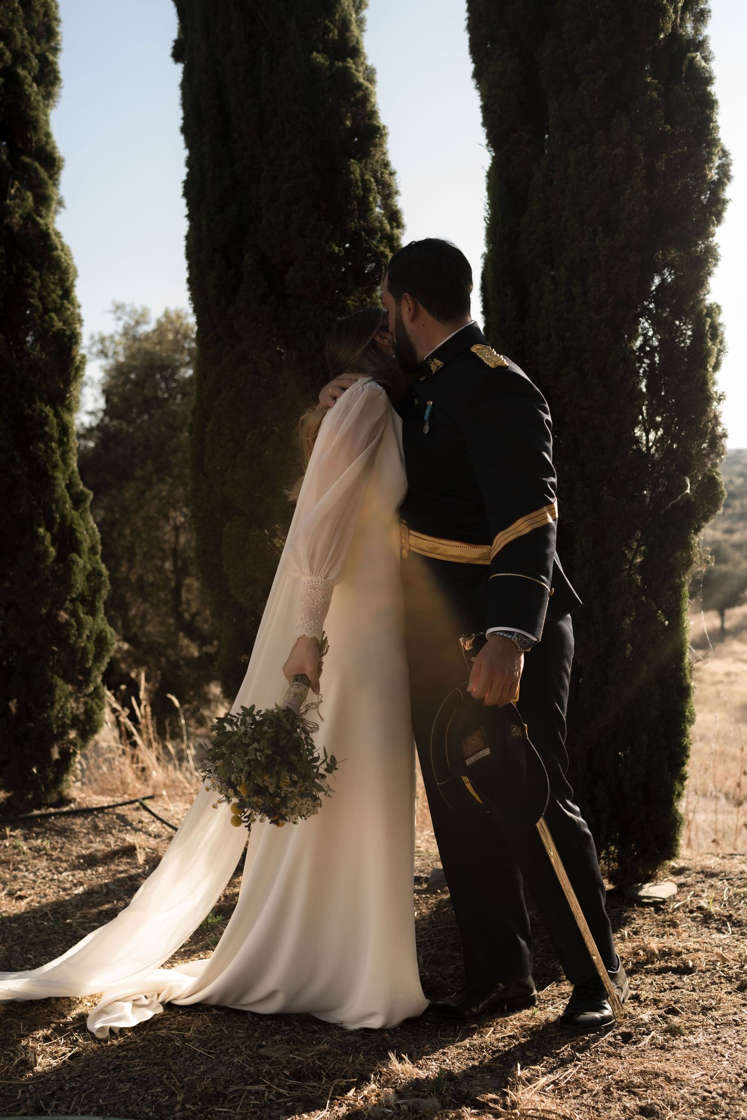 A couple poses among tall cypress trees in dramatic wedding day lighting.