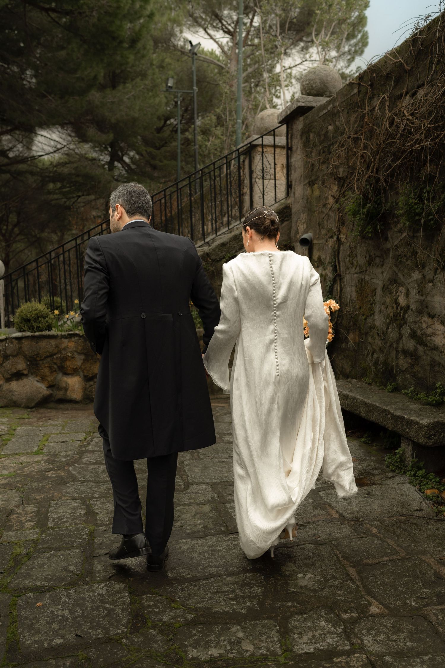 A couple walks up stone steps together in elegant wedding attire.