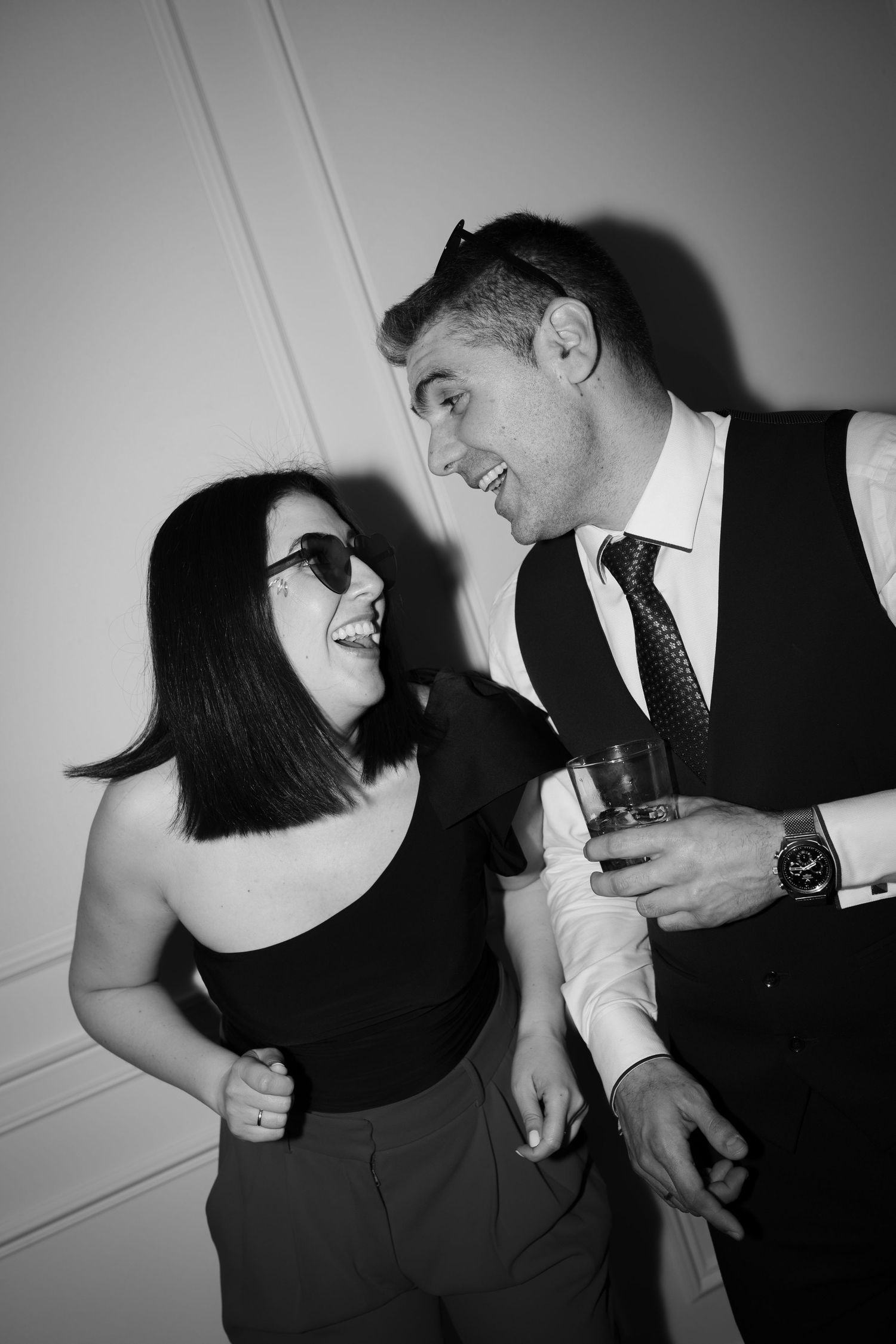 Two people laughing and dancing together in formal attire at a black and white party photo.