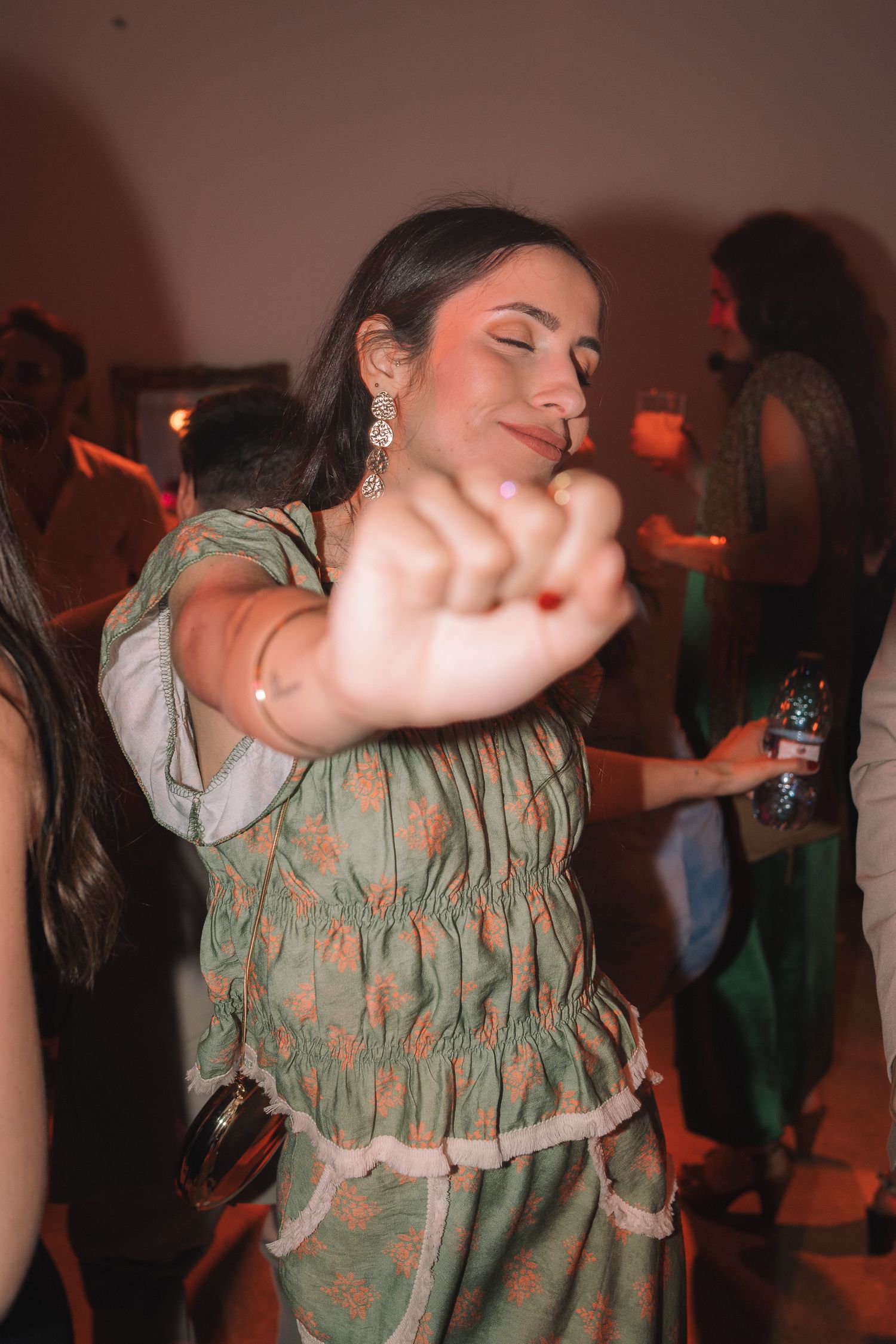 A person in a green patterned dress dances energetically at a party under dim lighting.
