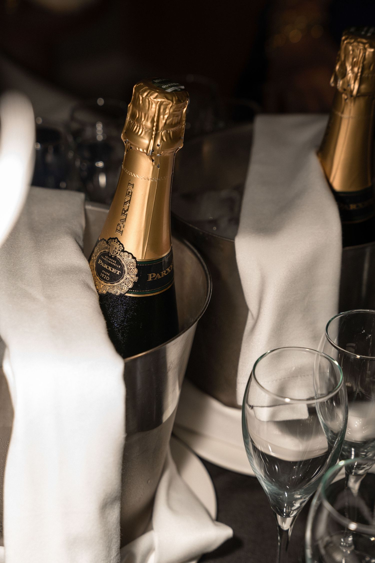 Champagne bottle in an ice bucket with empty glasses on white tablecloth.