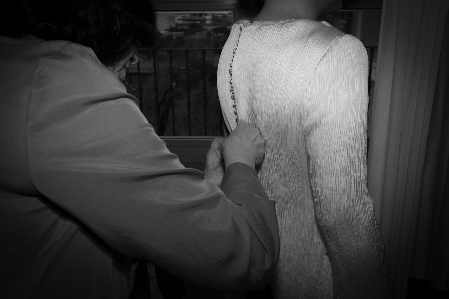 Black and white image of hands adjusting details on back of formal dress.