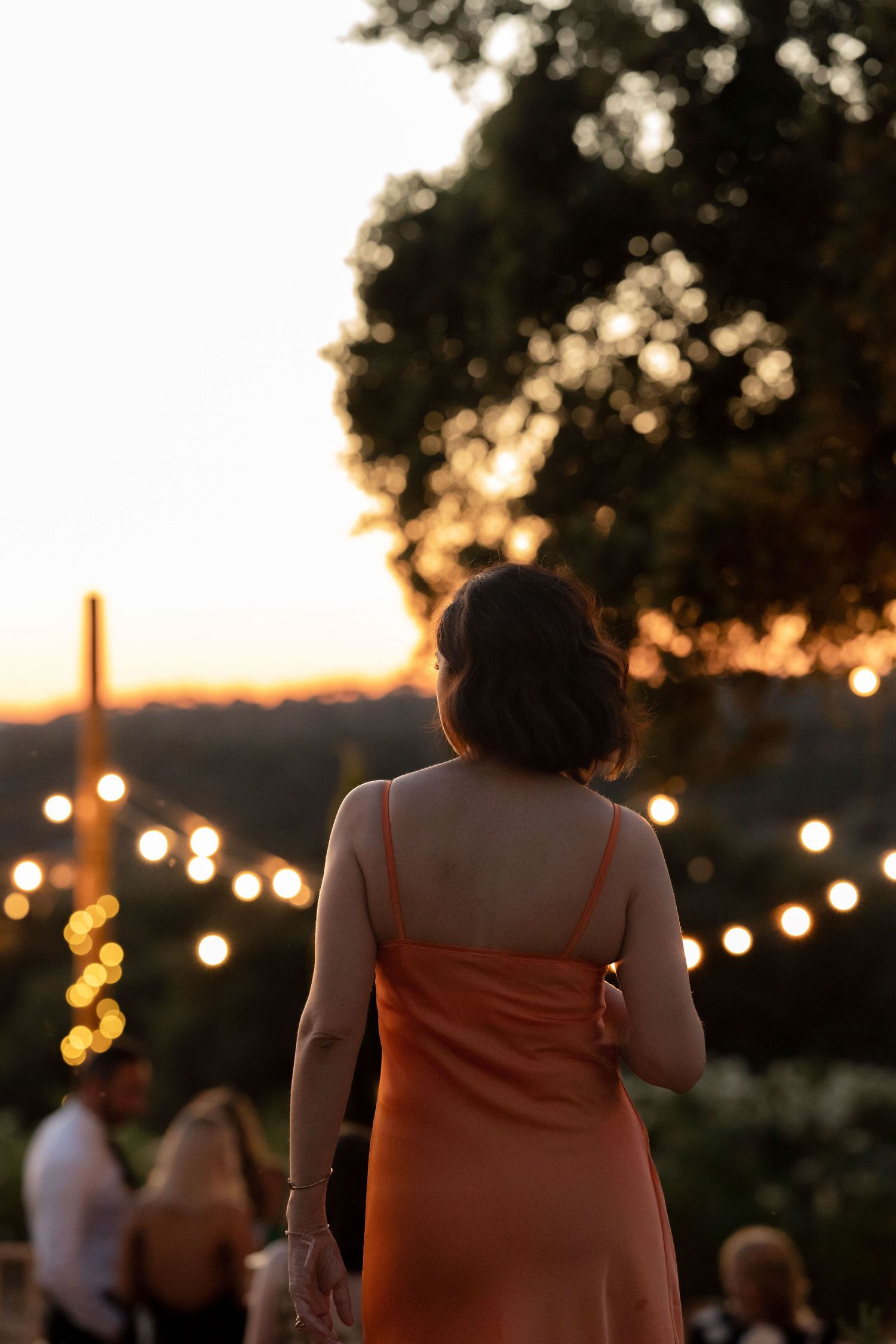 String lights illuminate an outdoor evening wedding reception as silhouettes move in the background.