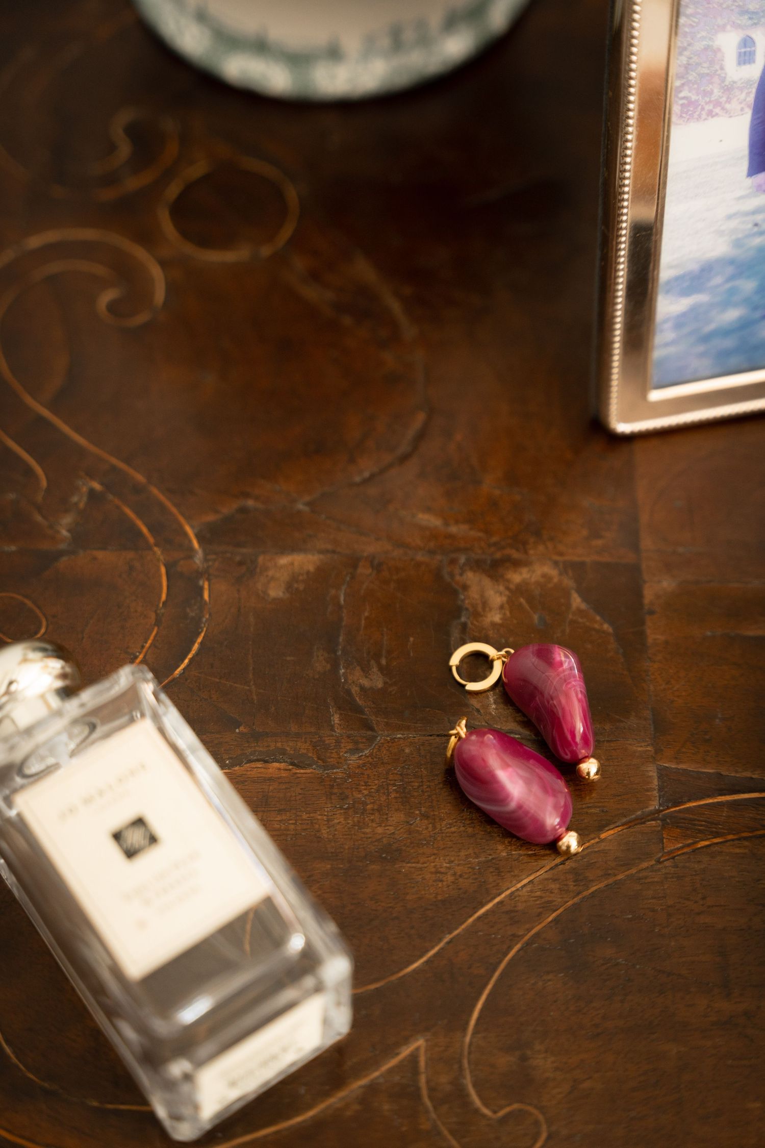 Perfume bottle and pink flower earrings arranged on dark wooden surface.