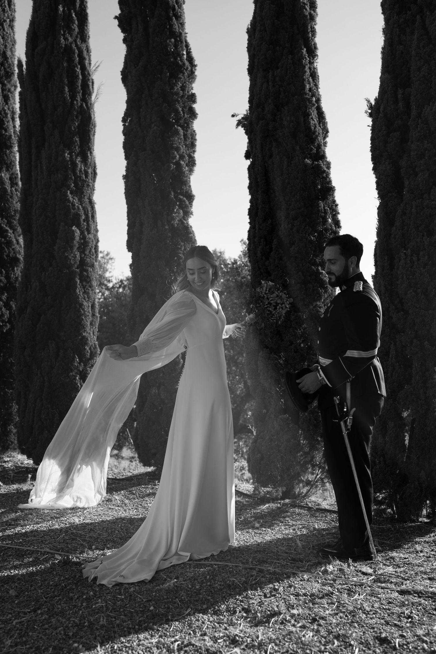 Black and white photo of newlyweds standing between majestic cypress trees.