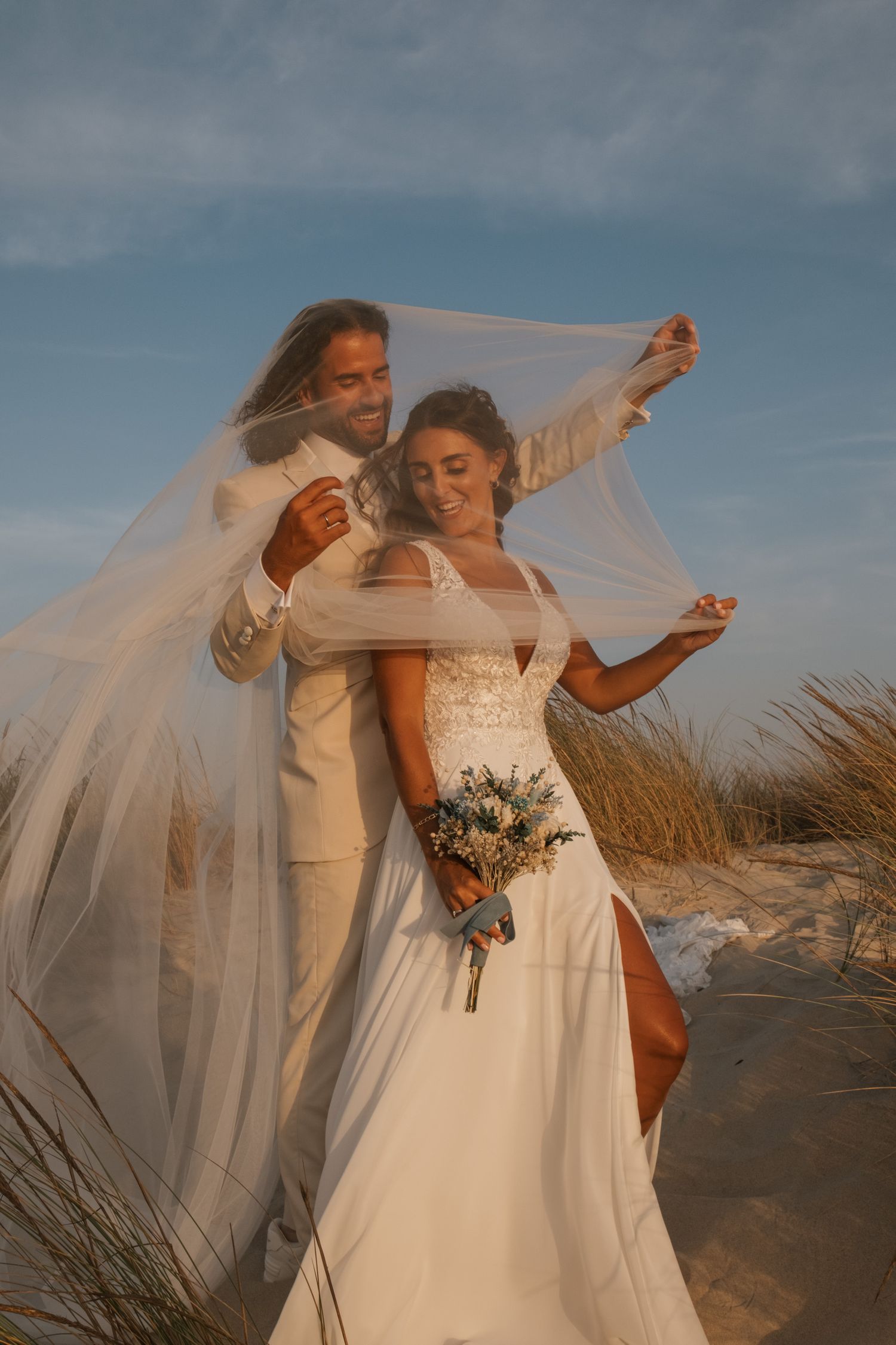 A romantic beach wedding photoshoot with flowing white dress and veil against the dunes.