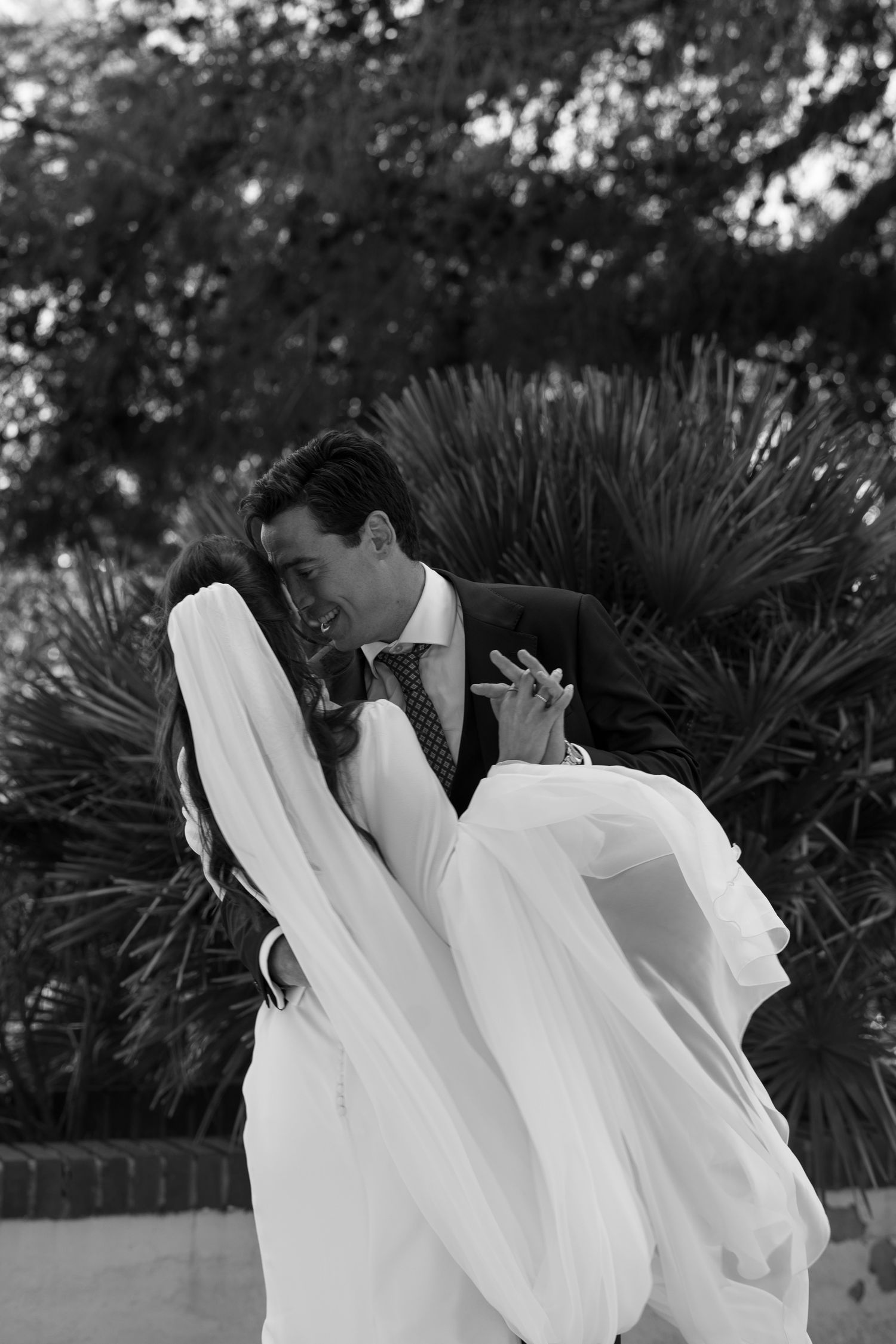 Black and white photo of a couple in wedding attire against a garden landscape.