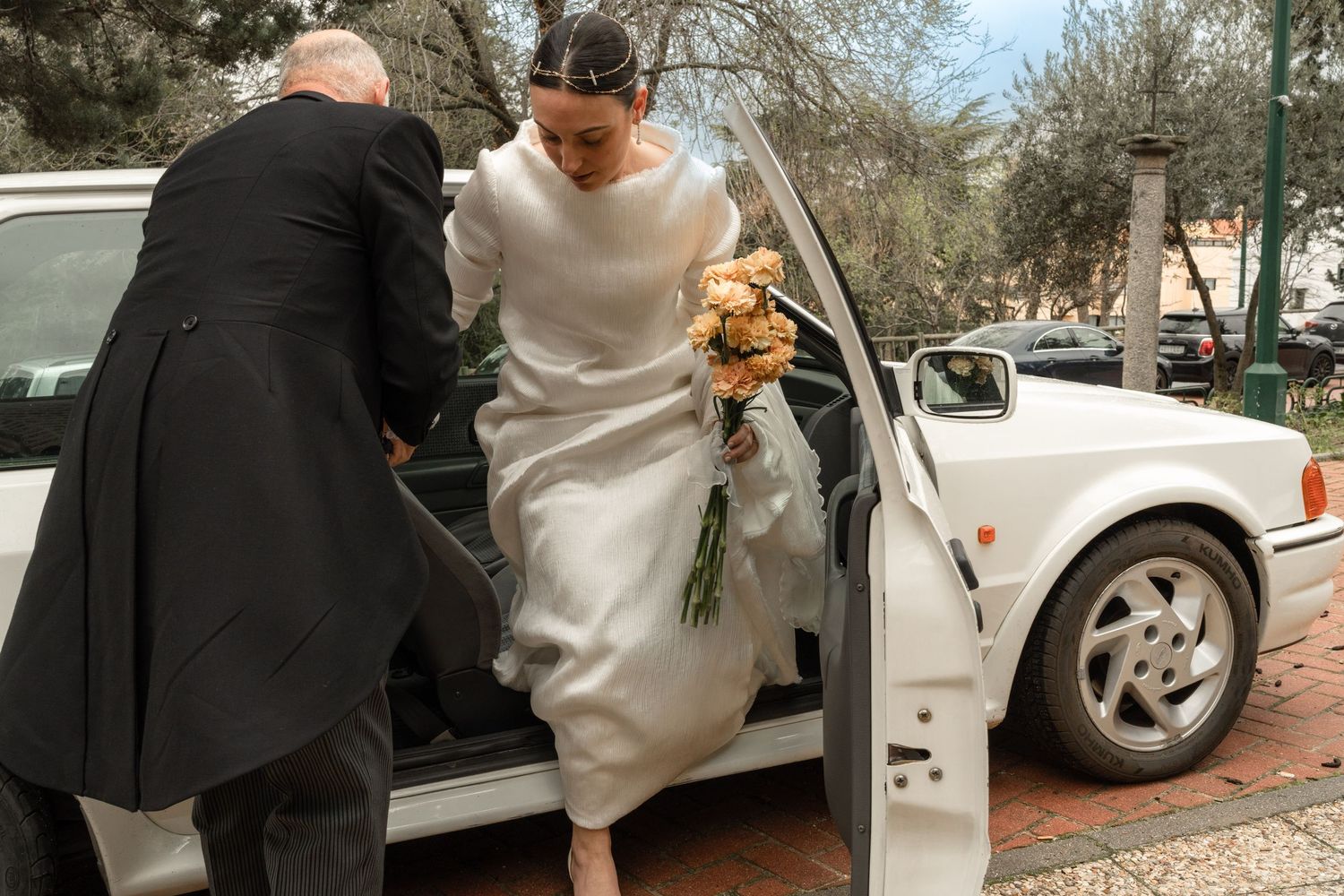 Getting into white wedding car with bouquet and formal attire.