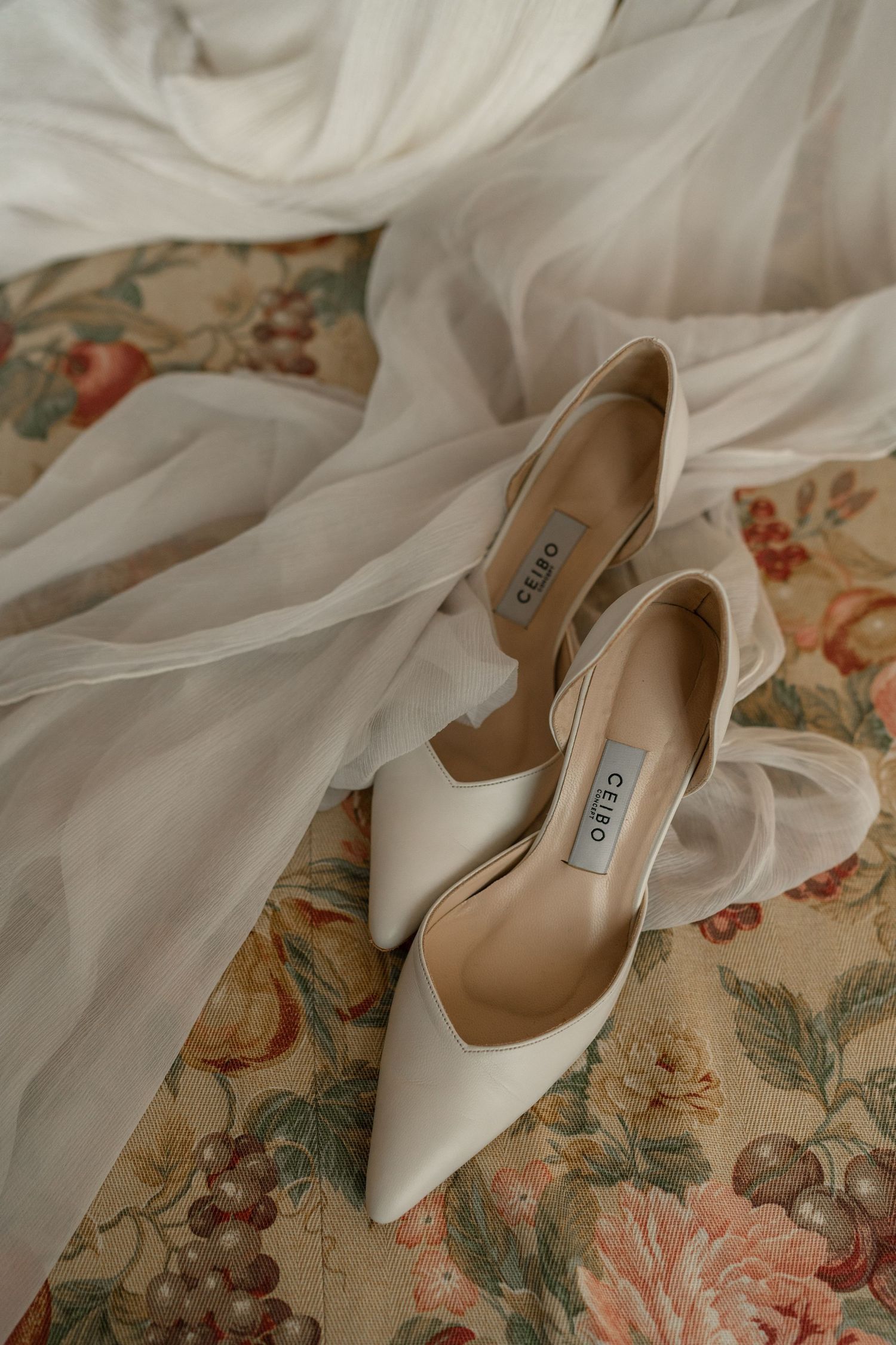 White bridal shoes on floral patterned fabric with flowing veil.