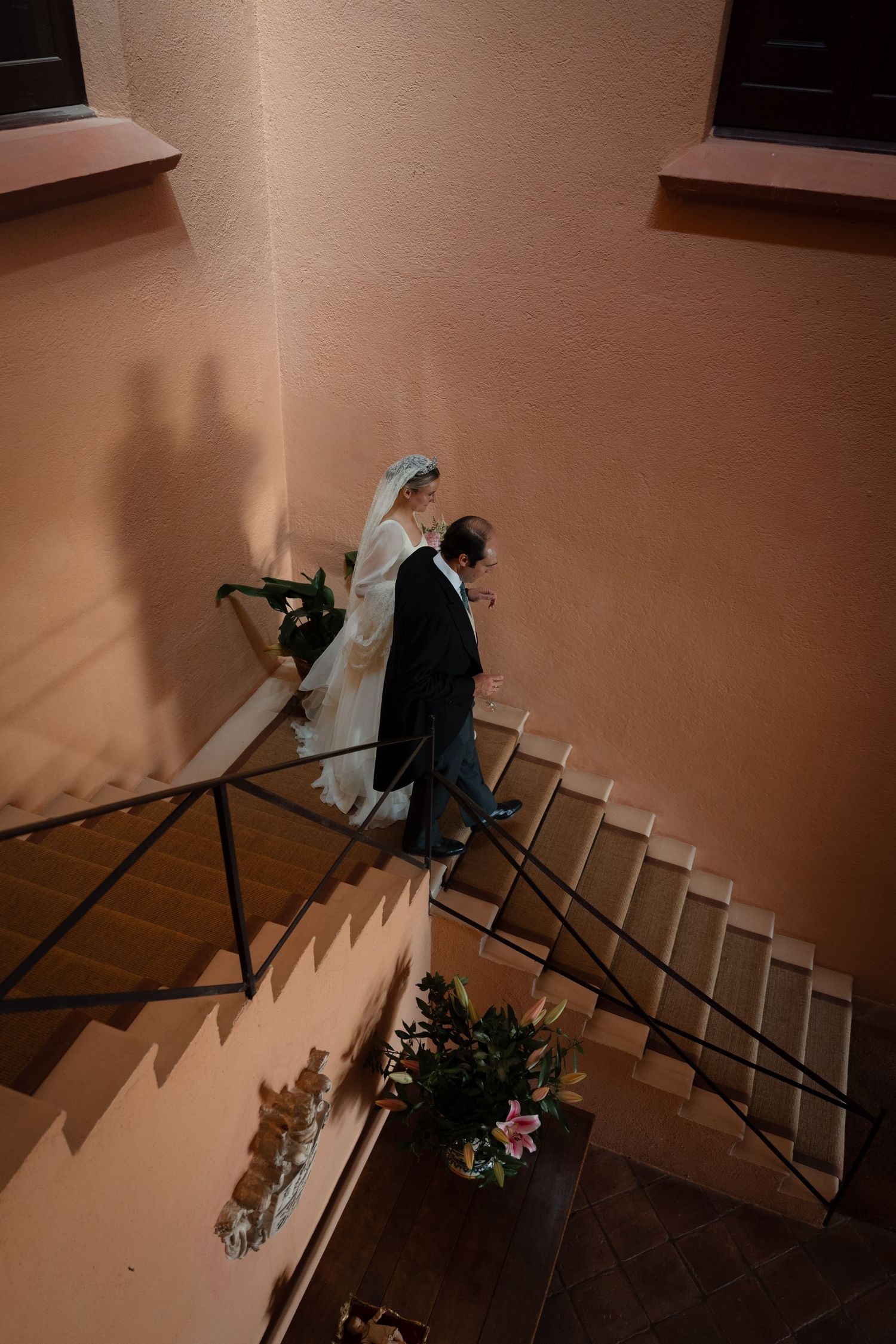 A couple walks down stairs casting dramatic shadows on a peach-colored wall.