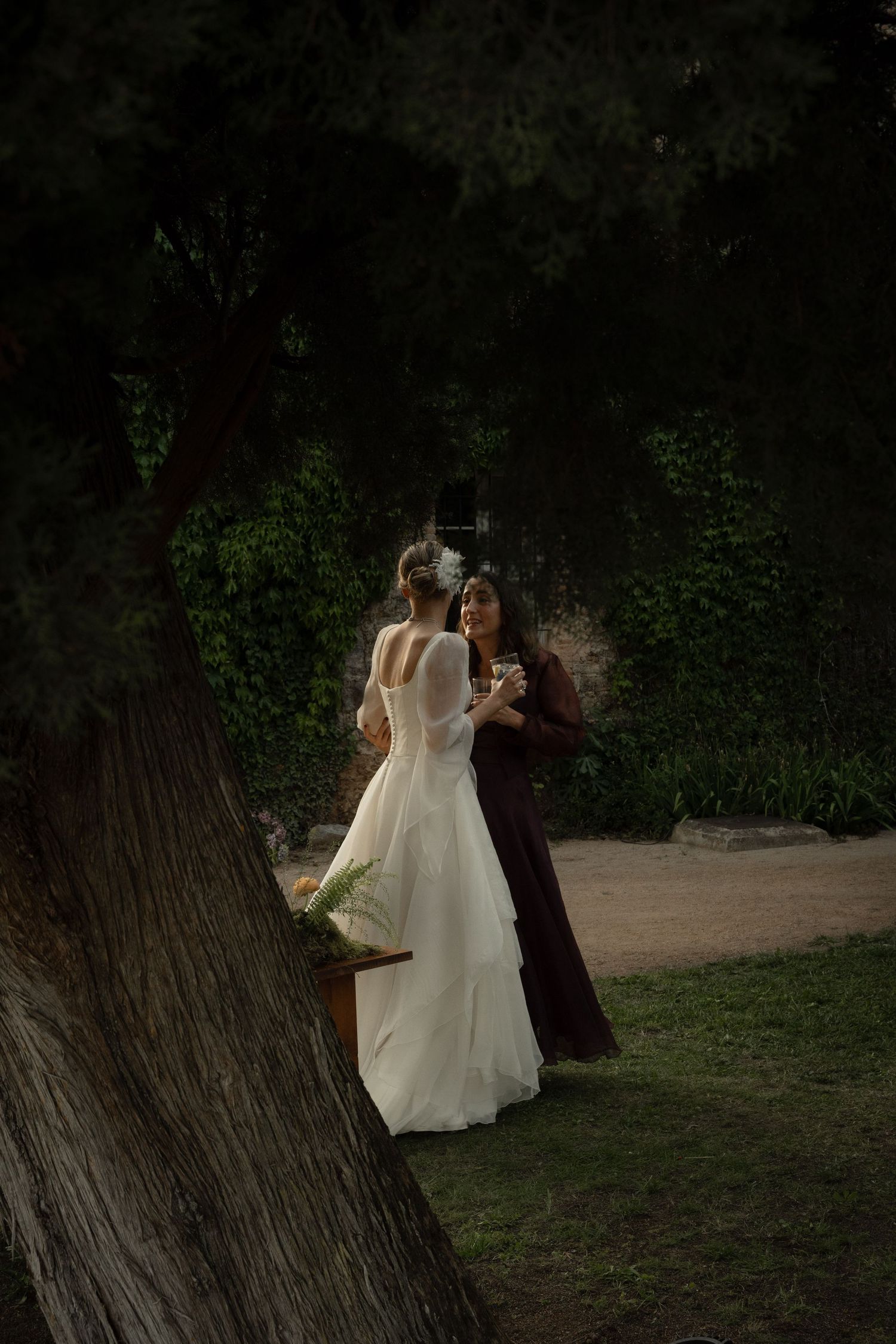 Evening outdoor celebration with people in formal attire walking through a garden setting.