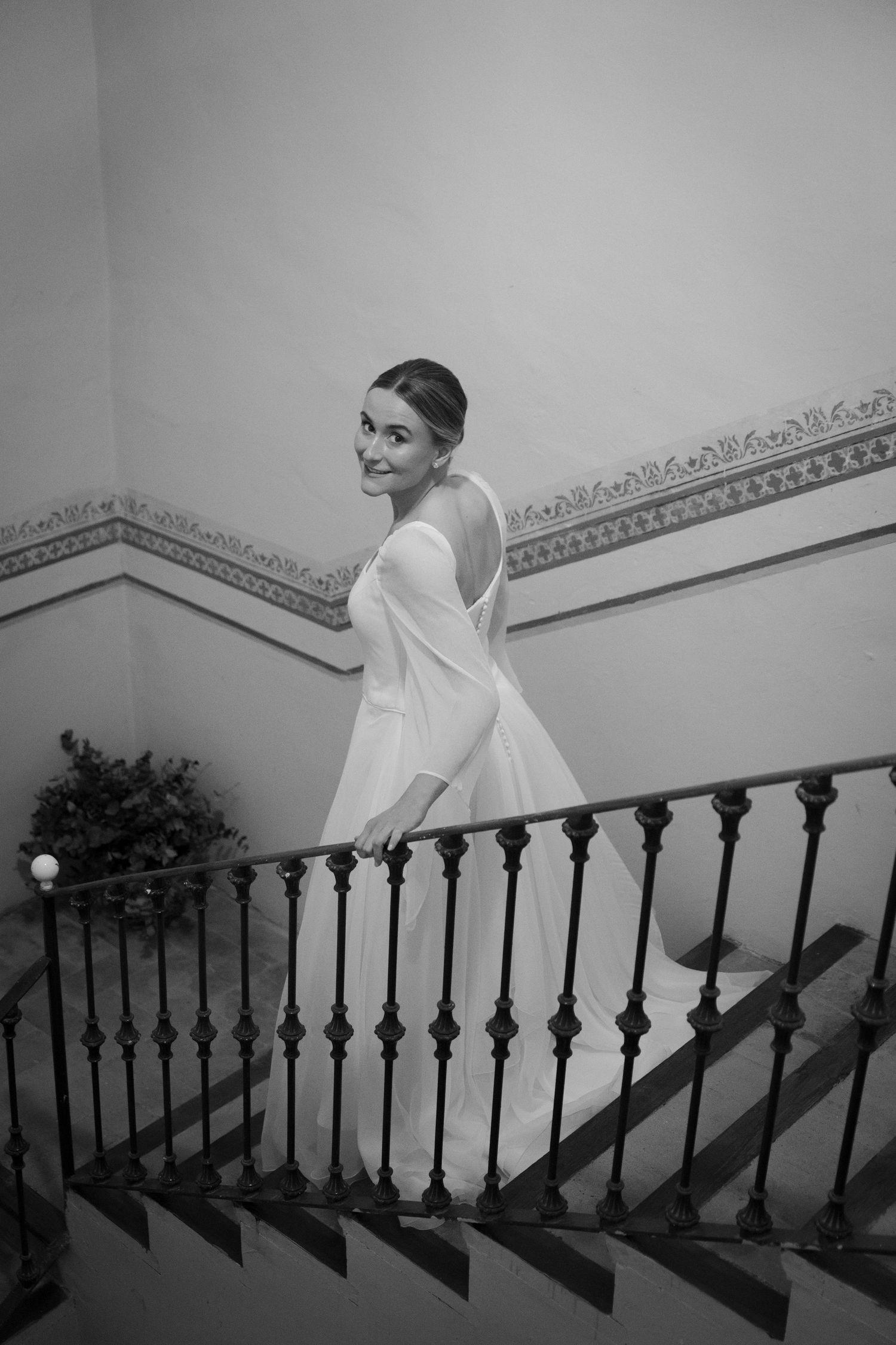 Black and white photo of bride on elegant staircase with ornate railing.