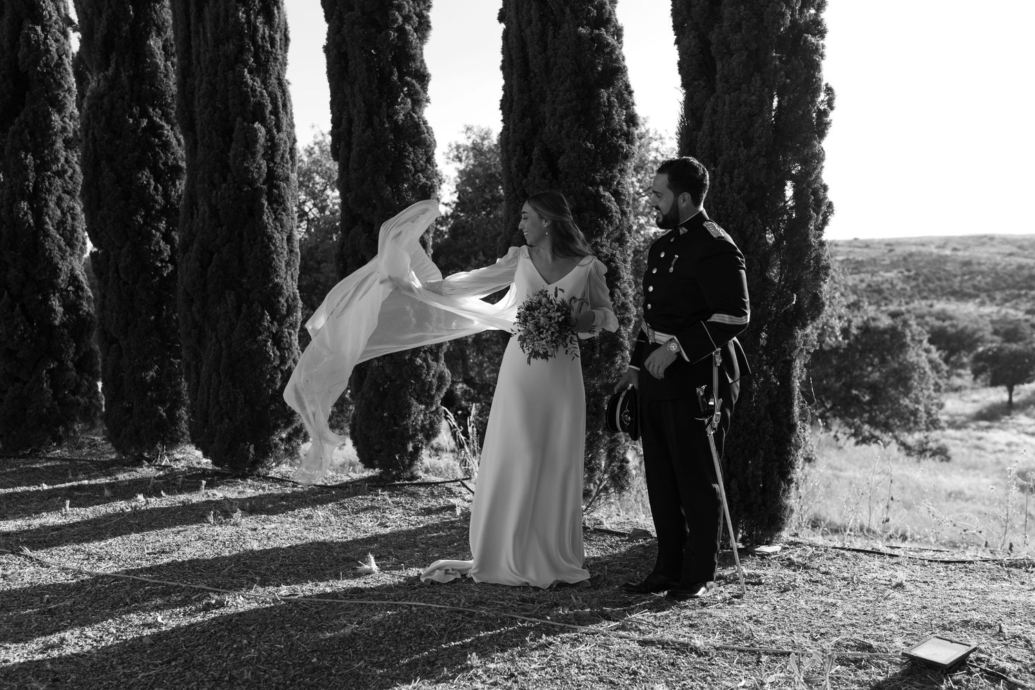 Wedding party poses between dramatic rows of cypress trees in natural lighting.