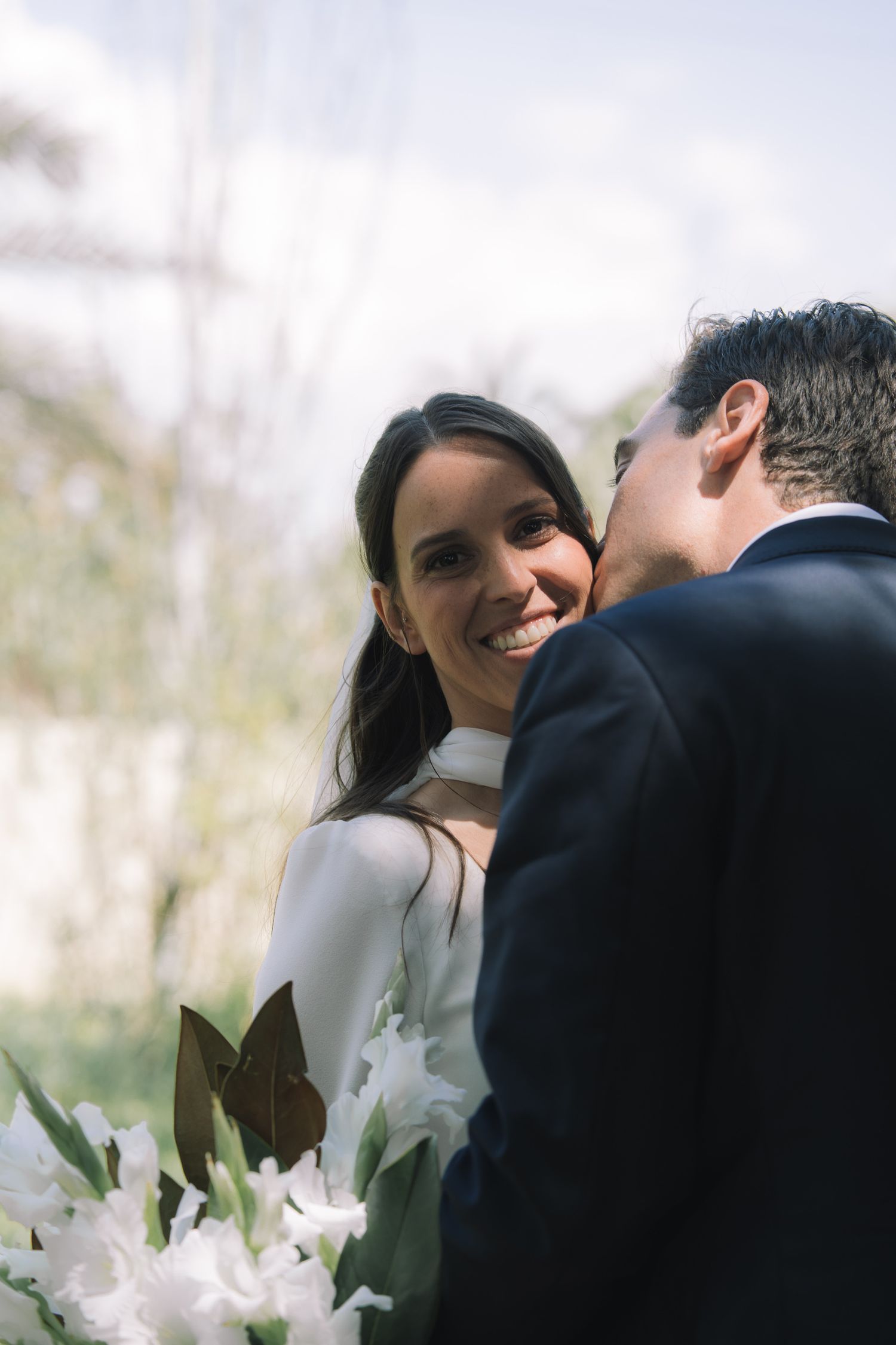 A tender moment between newlyweds surrounded by white flowers in natural lighting.