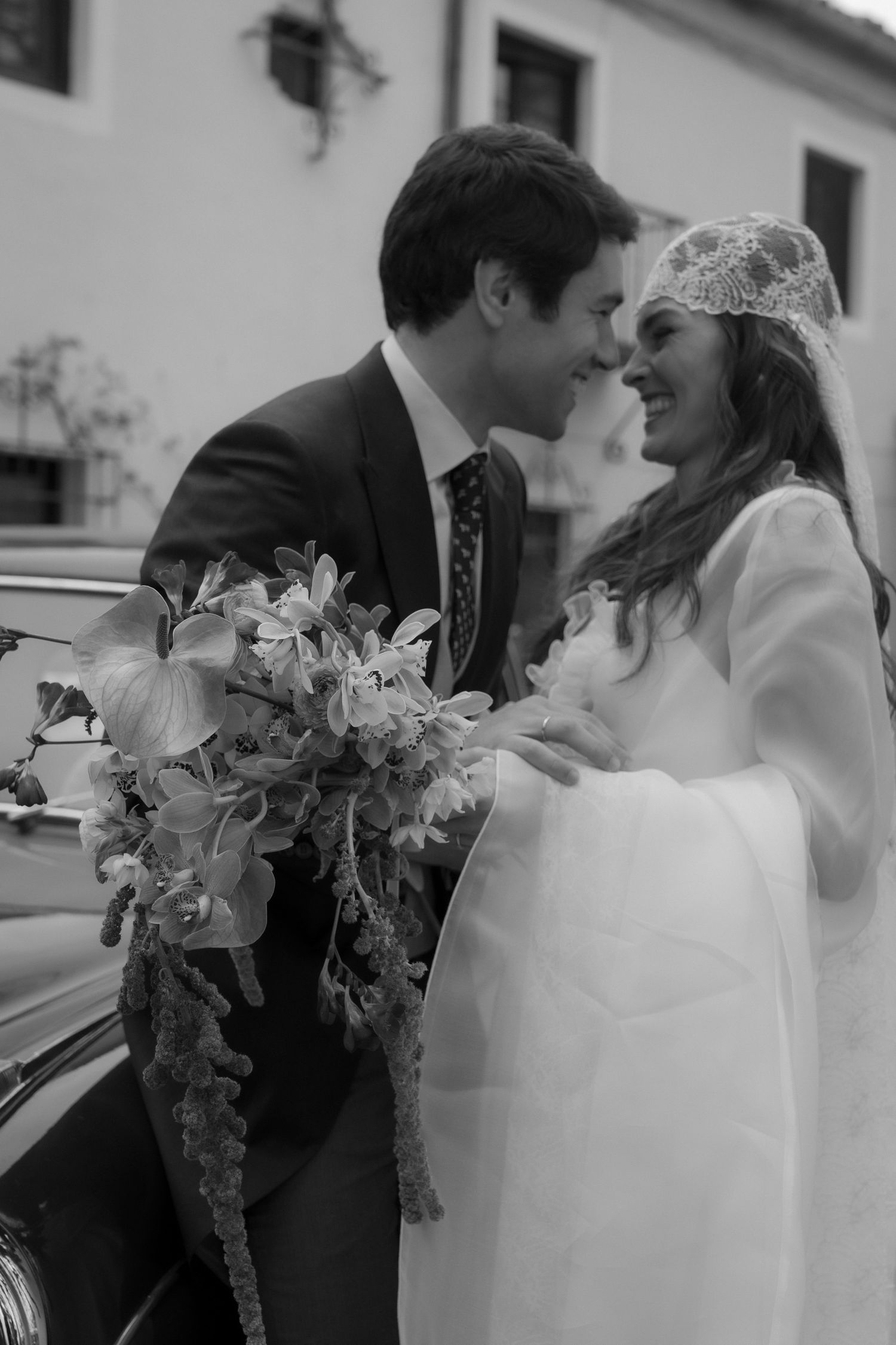 A romantic black and white wedding photo showing a tender moment between newlyweds with a beautiful floral bouquet.