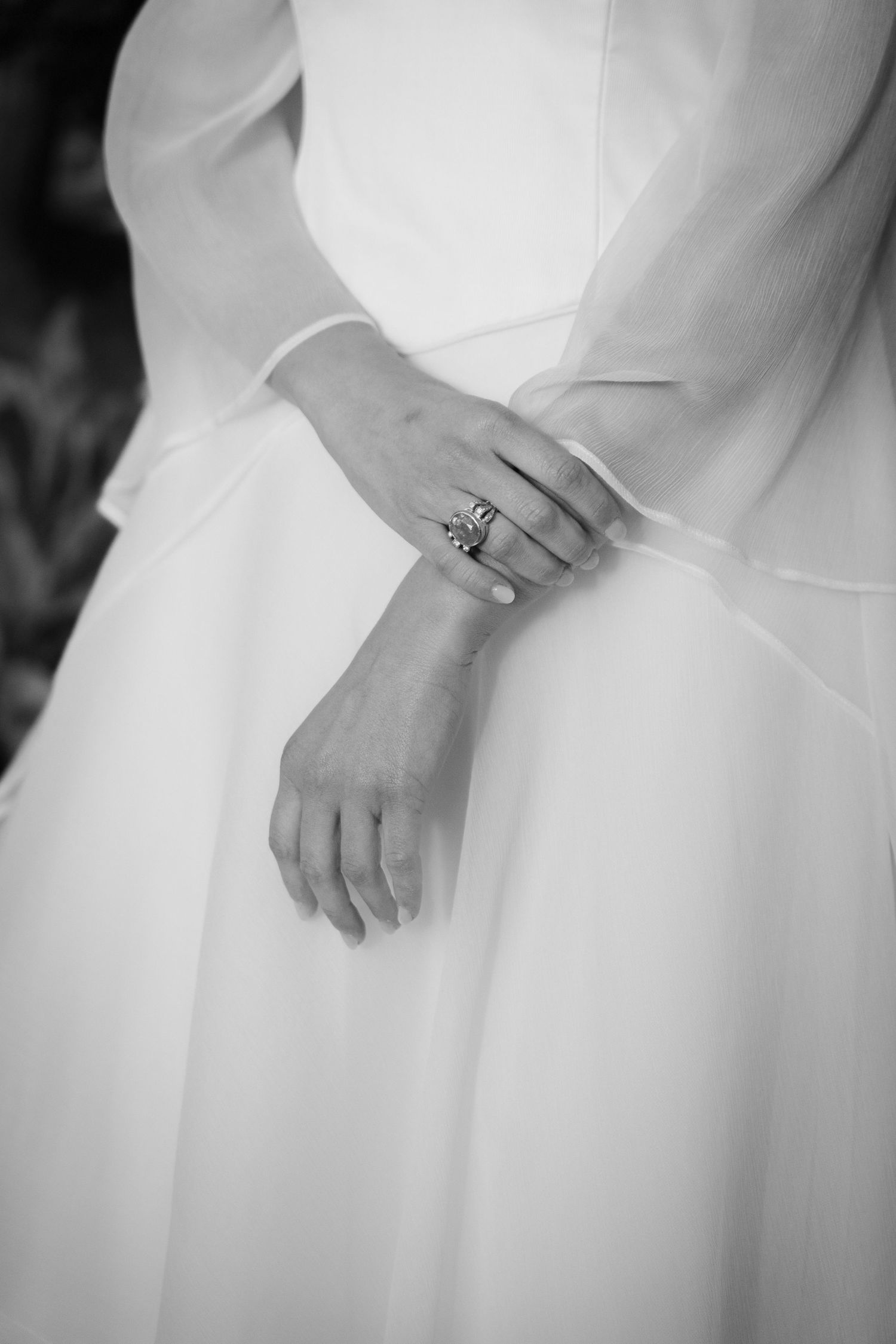 Close-up black and white photo of hands in white wedding dress fabric with an elegant ring.