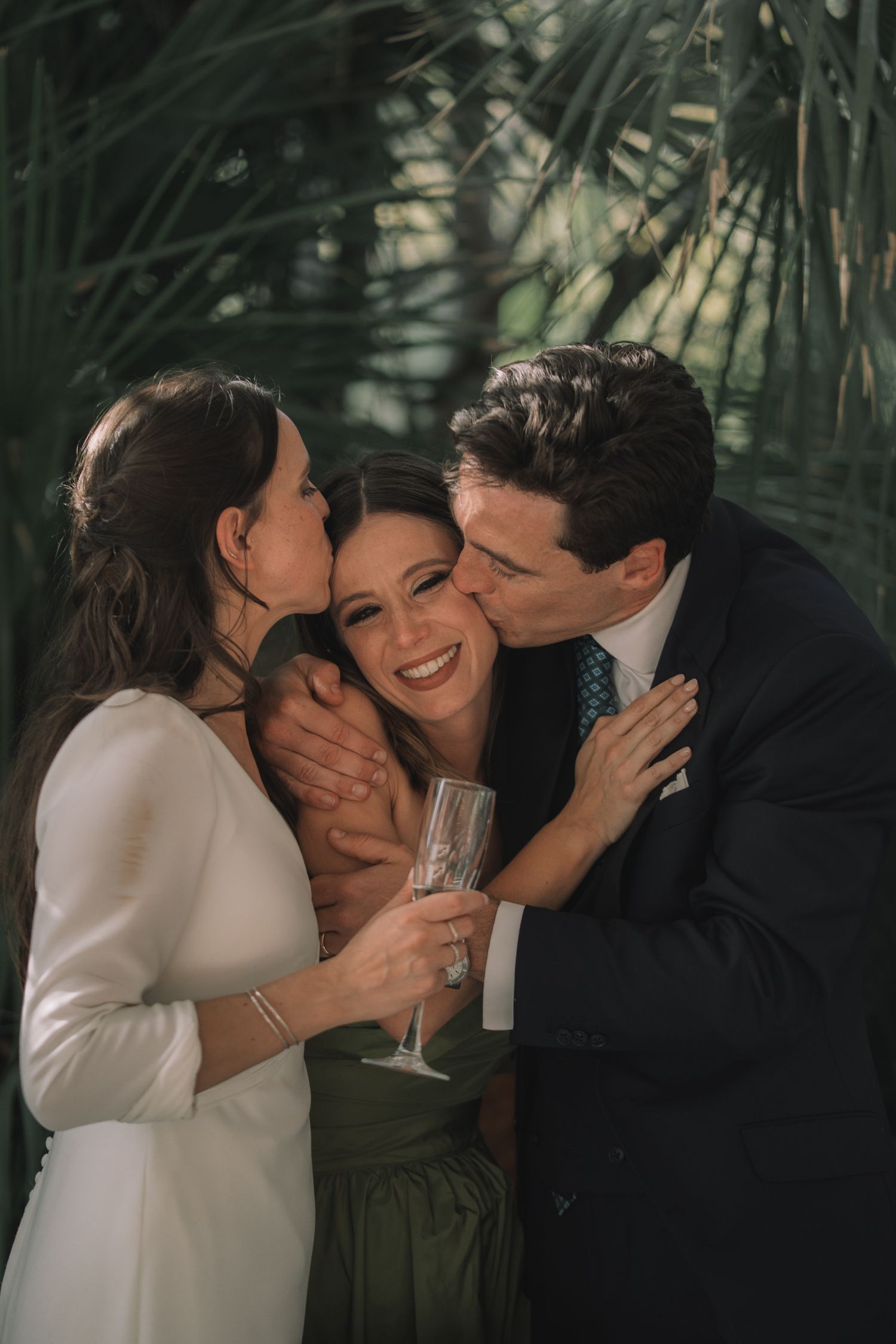 Wedding party shares intimate laughs and embraces against a backdrop of palm fronds.