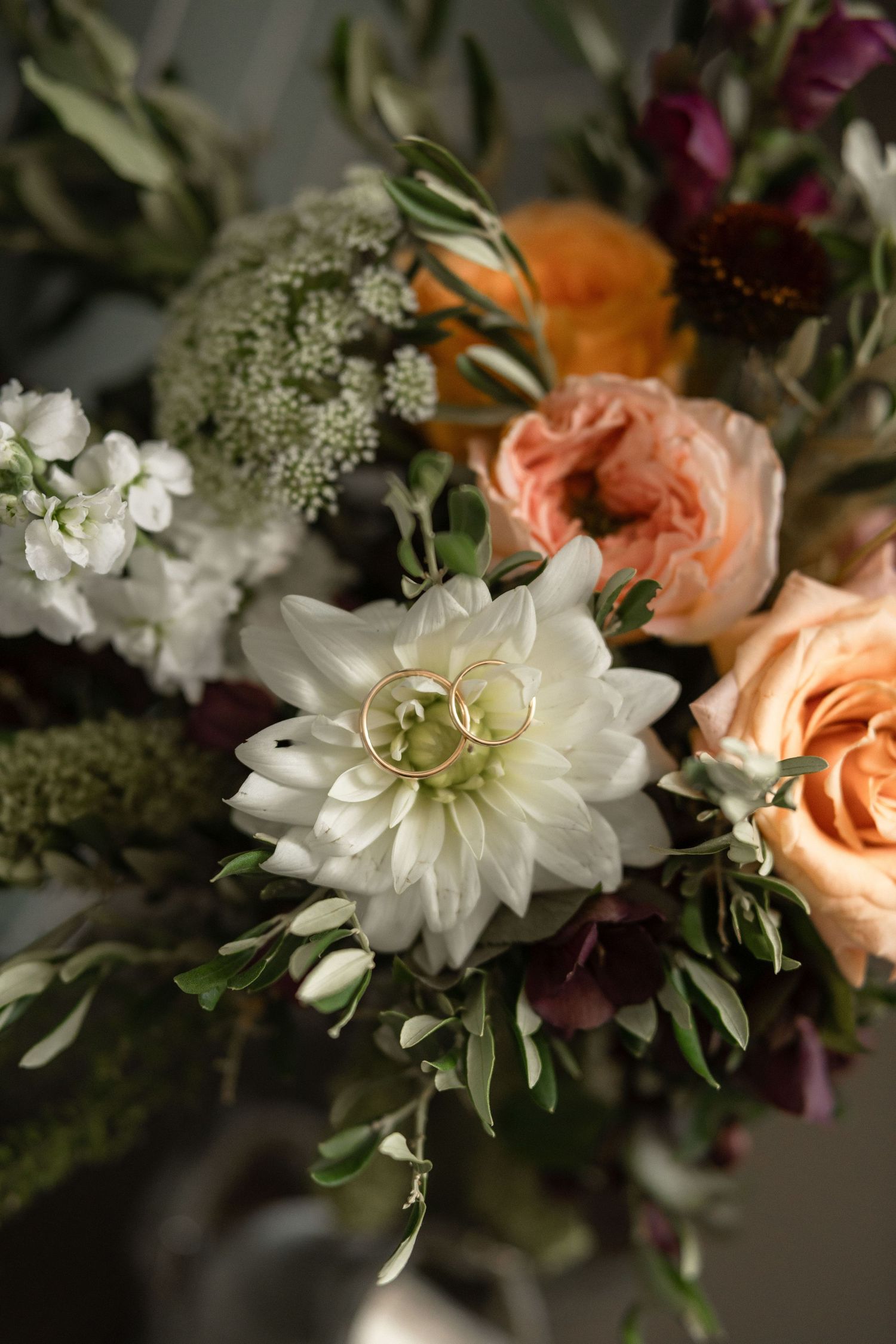 Wedding bouquet with white dahlia, peach roses, and mixed flowers against dark background.