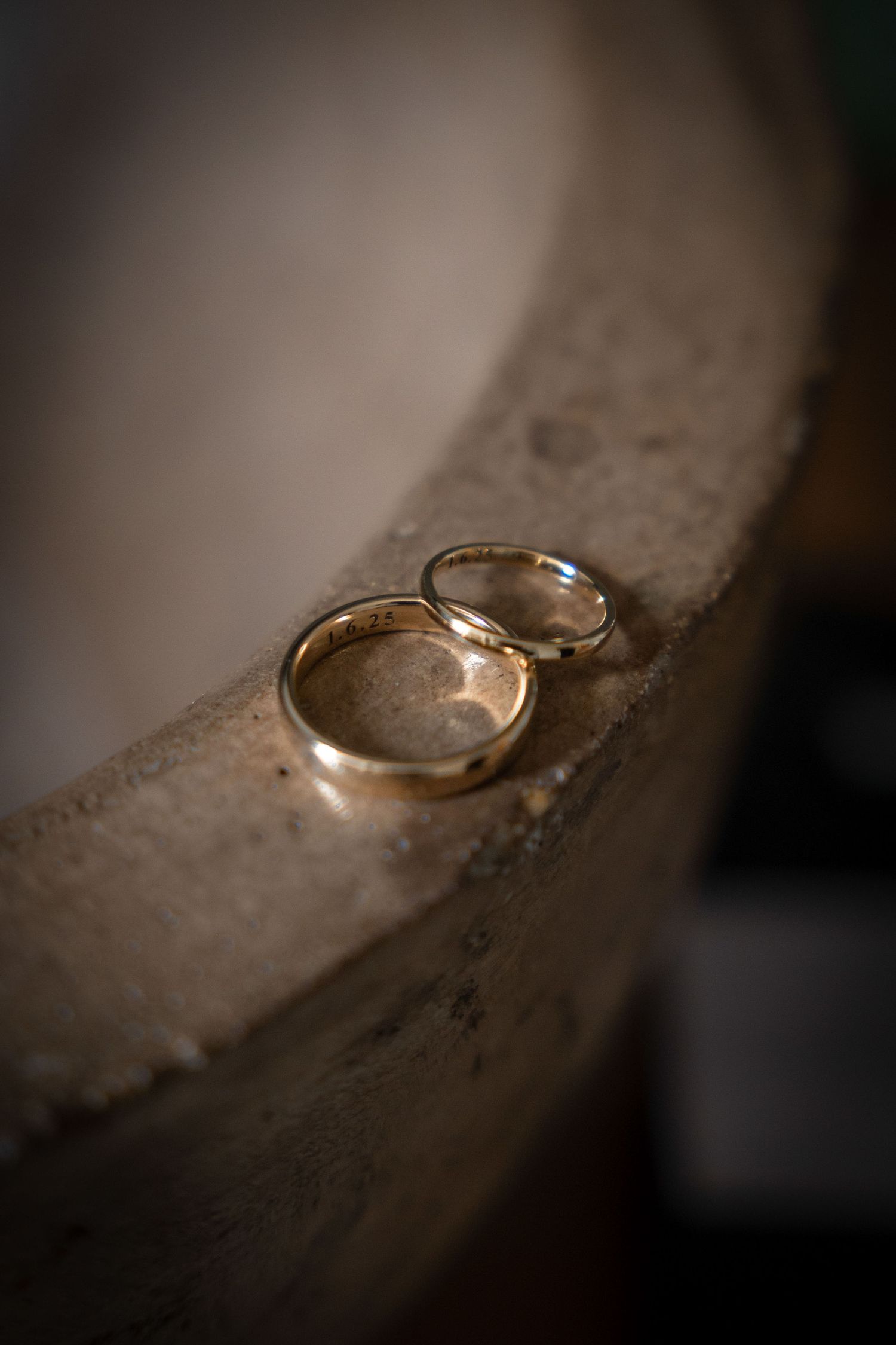 Two gold wedding rings sitting on a textured concrete surface in moody lighting.