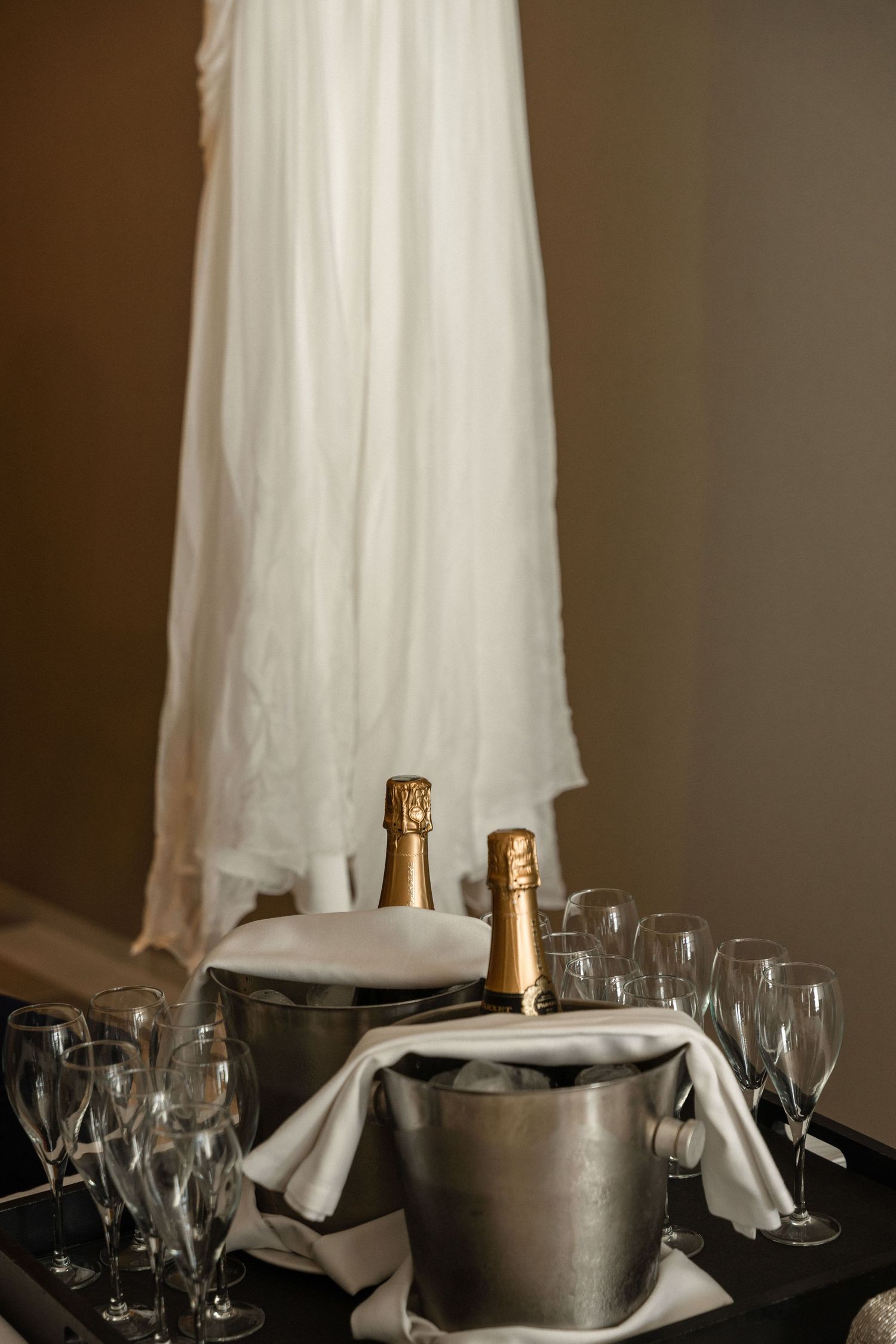 Elegant wedding reception setup with champagne bucket and wine glasses against white fabric.