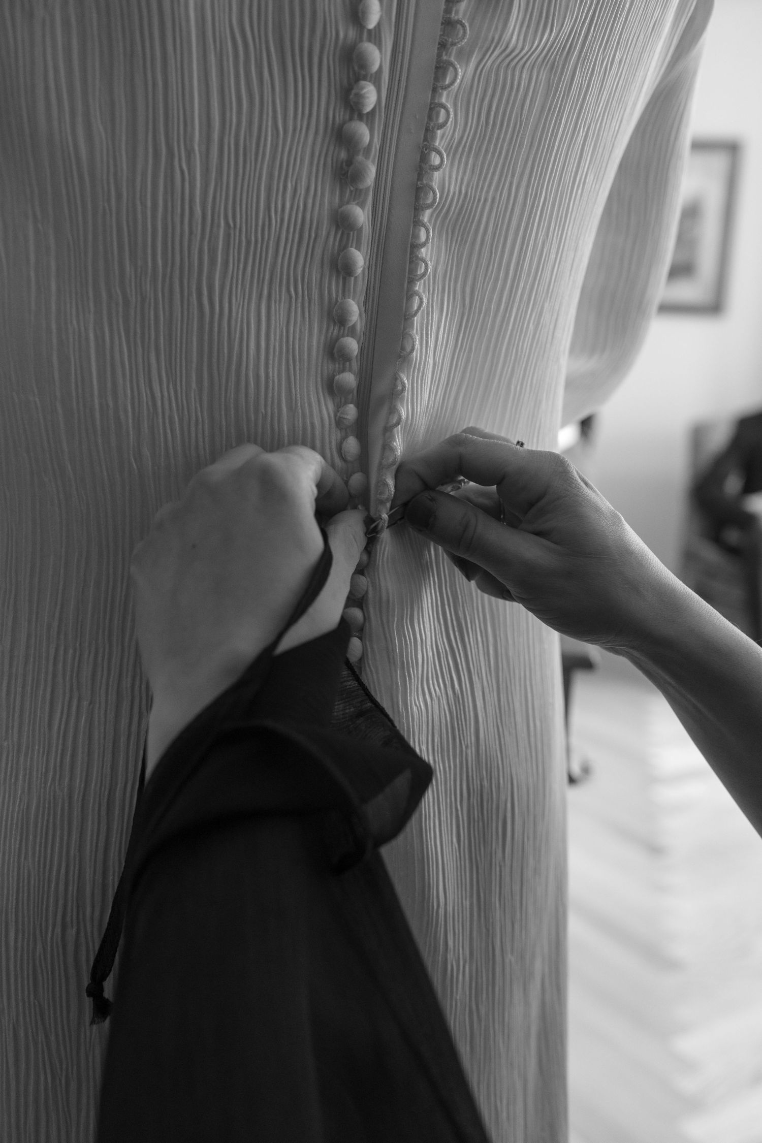 Hands fastening delicate button details on back of white textured dress.